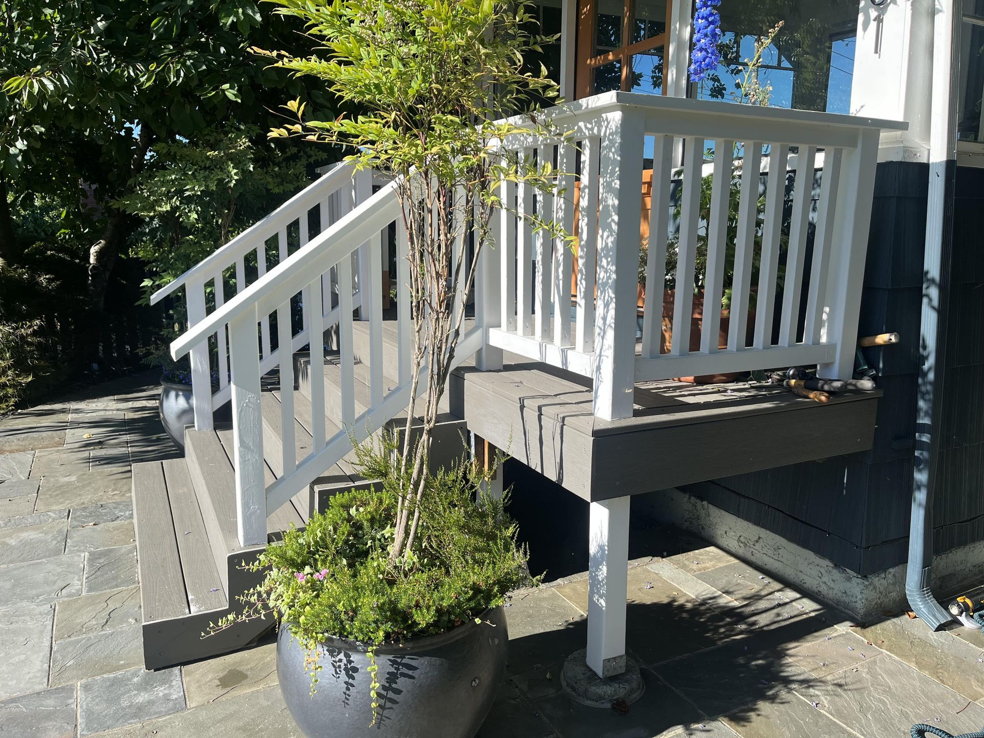 Small porch with white railings, gray steps, and a potted plant in front of a house.