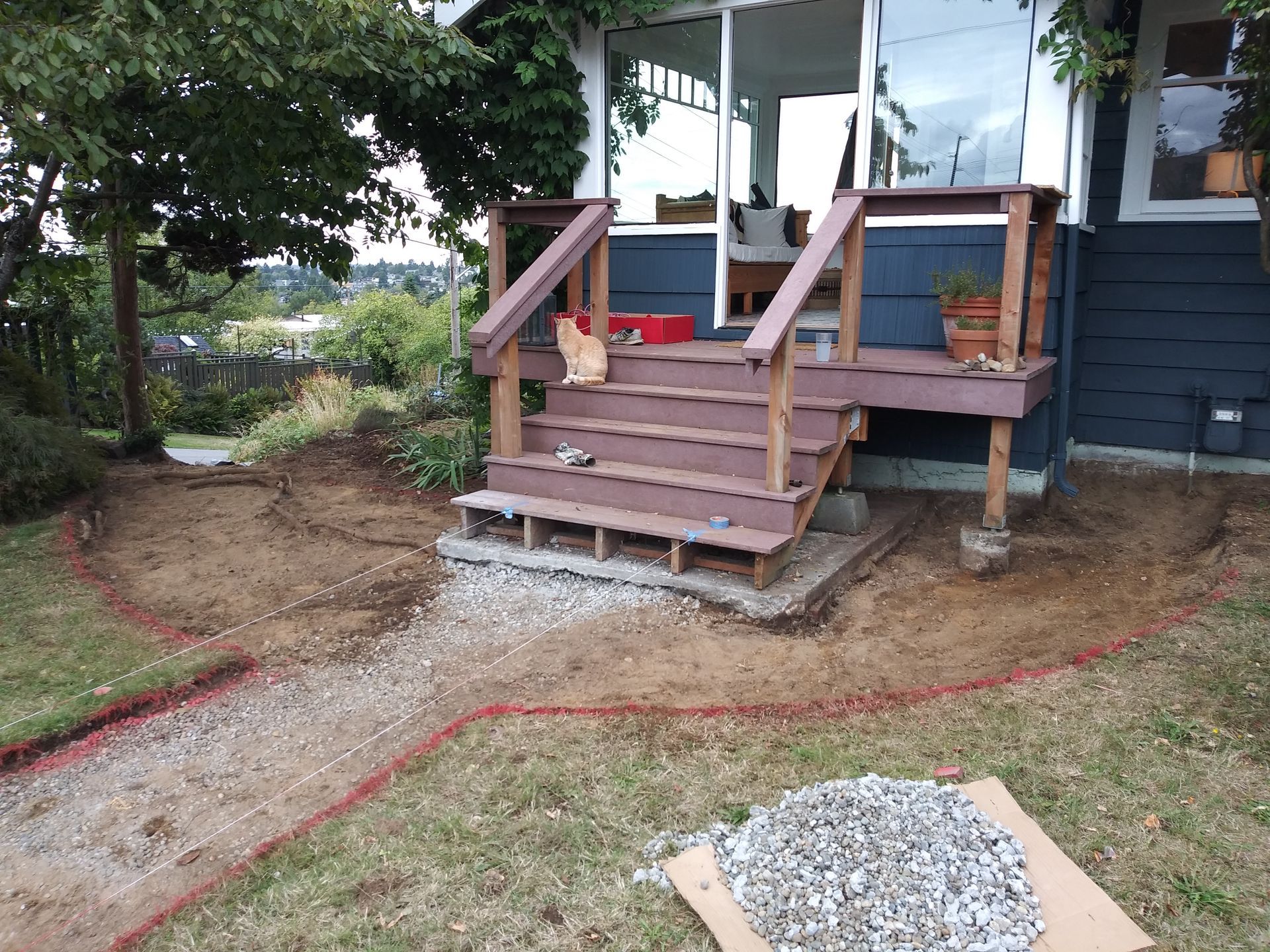 Front porch with wooden steps, red handrails, and a dirt yard with gravel piles beside a dark house.