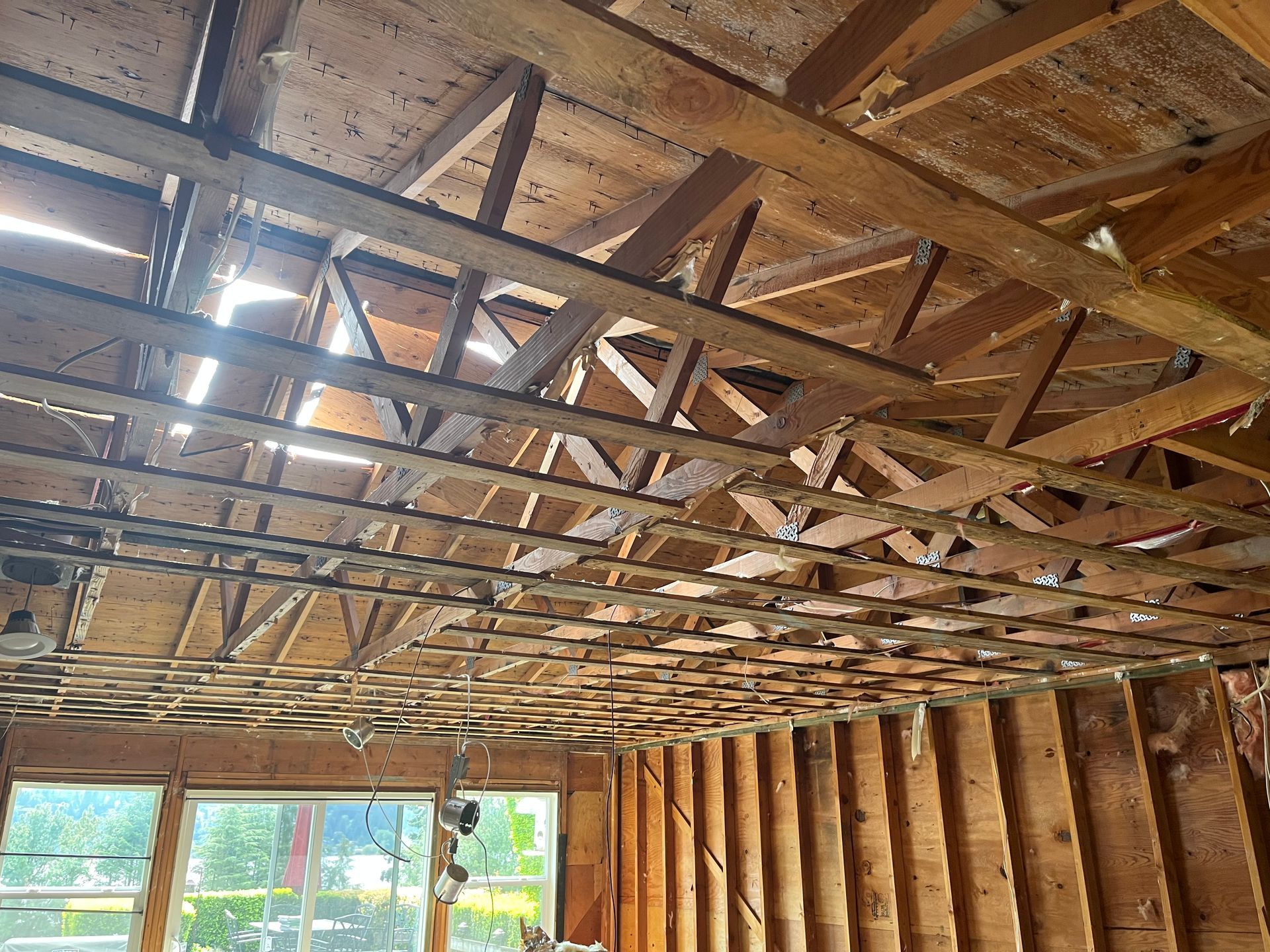 Wooden roof trusses and beams inside an unfinished room with exposed wall studs and windows below.