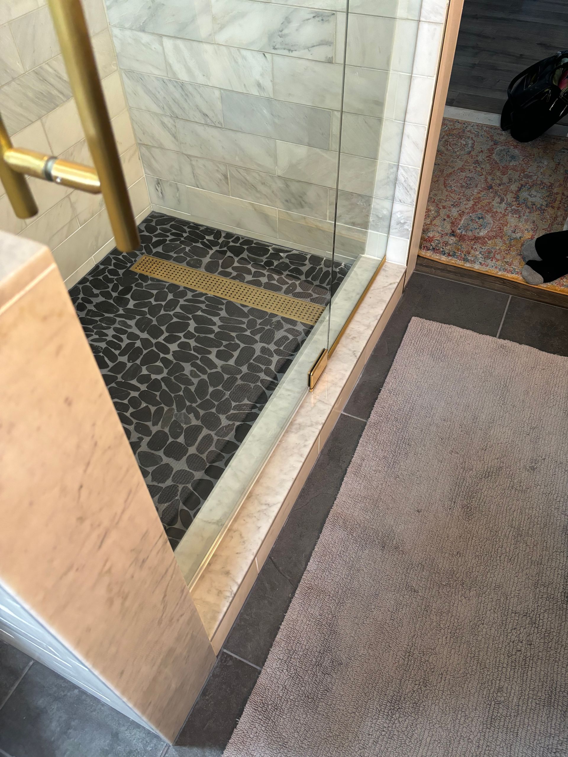 Tiled shower entrance with glass door, stone wall, and patterned bath mat beside it