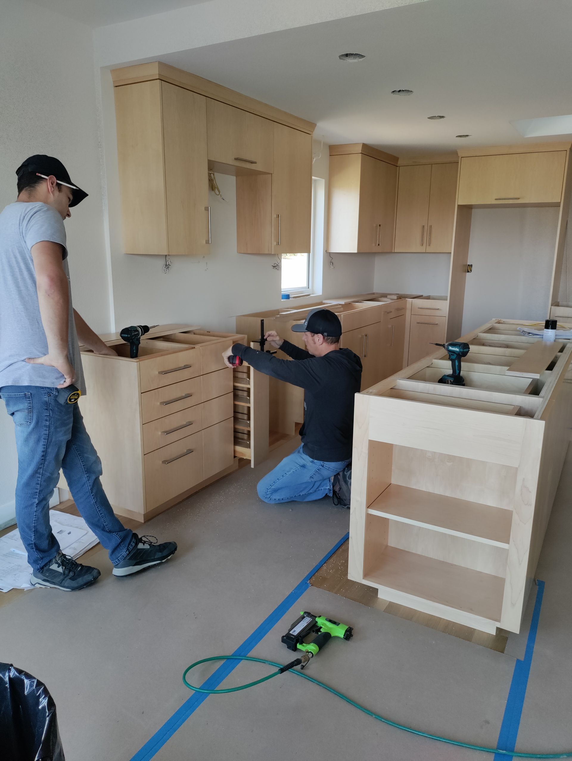 Workers installing light wood kitchen cabinets in a bright room.