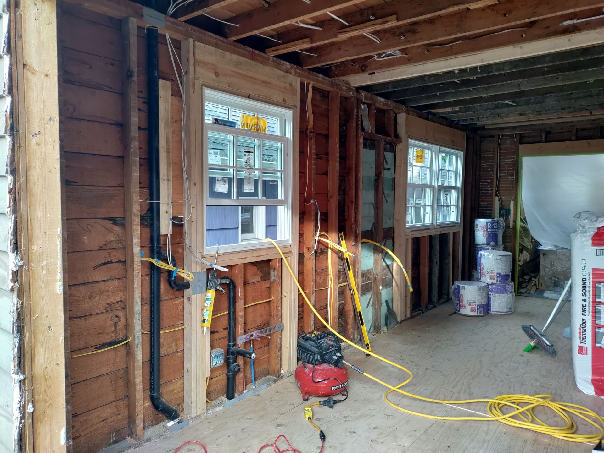 Interior of a house under renovation with exposed studs, windows, and construction tools on the floor.