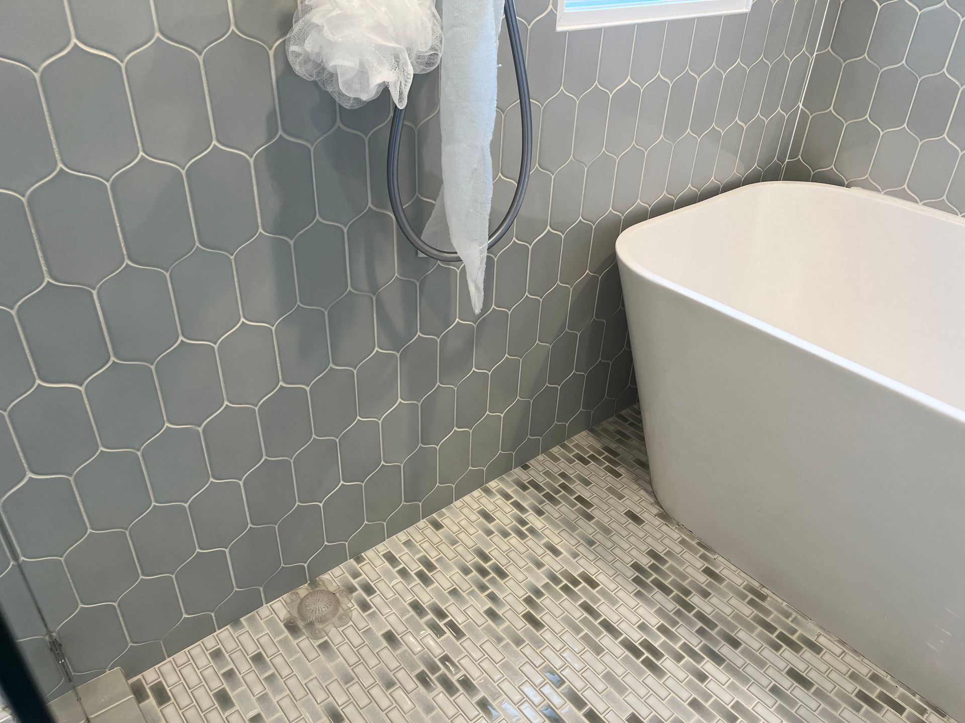 Modern bathroom corner with gray hex tile, speckled floor, and white bathtub edge