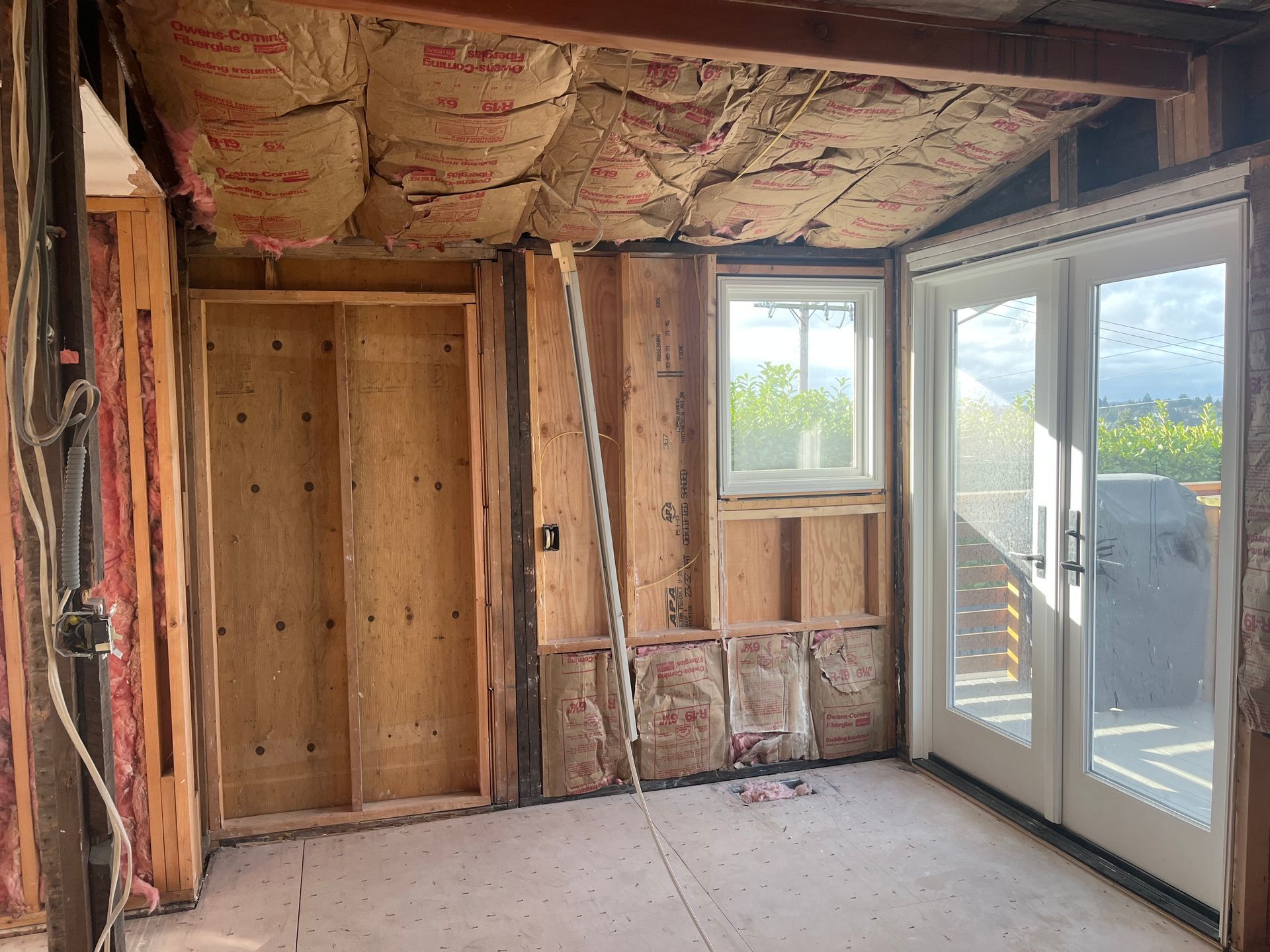 Partially renovated room with exposed insulation, unfinished walls, and a glass door to a deck