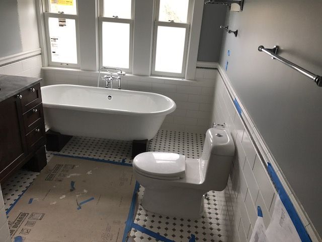 Accessible bathroom with bathtub, toilet, grab bar, and blue painter’s tape on the floor and walls