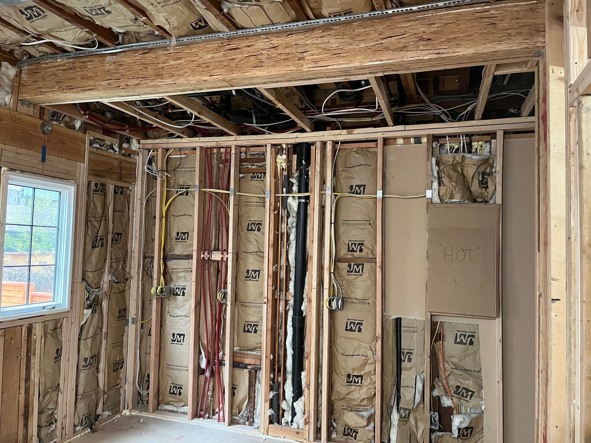 Unfinished room with exposed wooden framing, insulation, drywall patches, and a window.