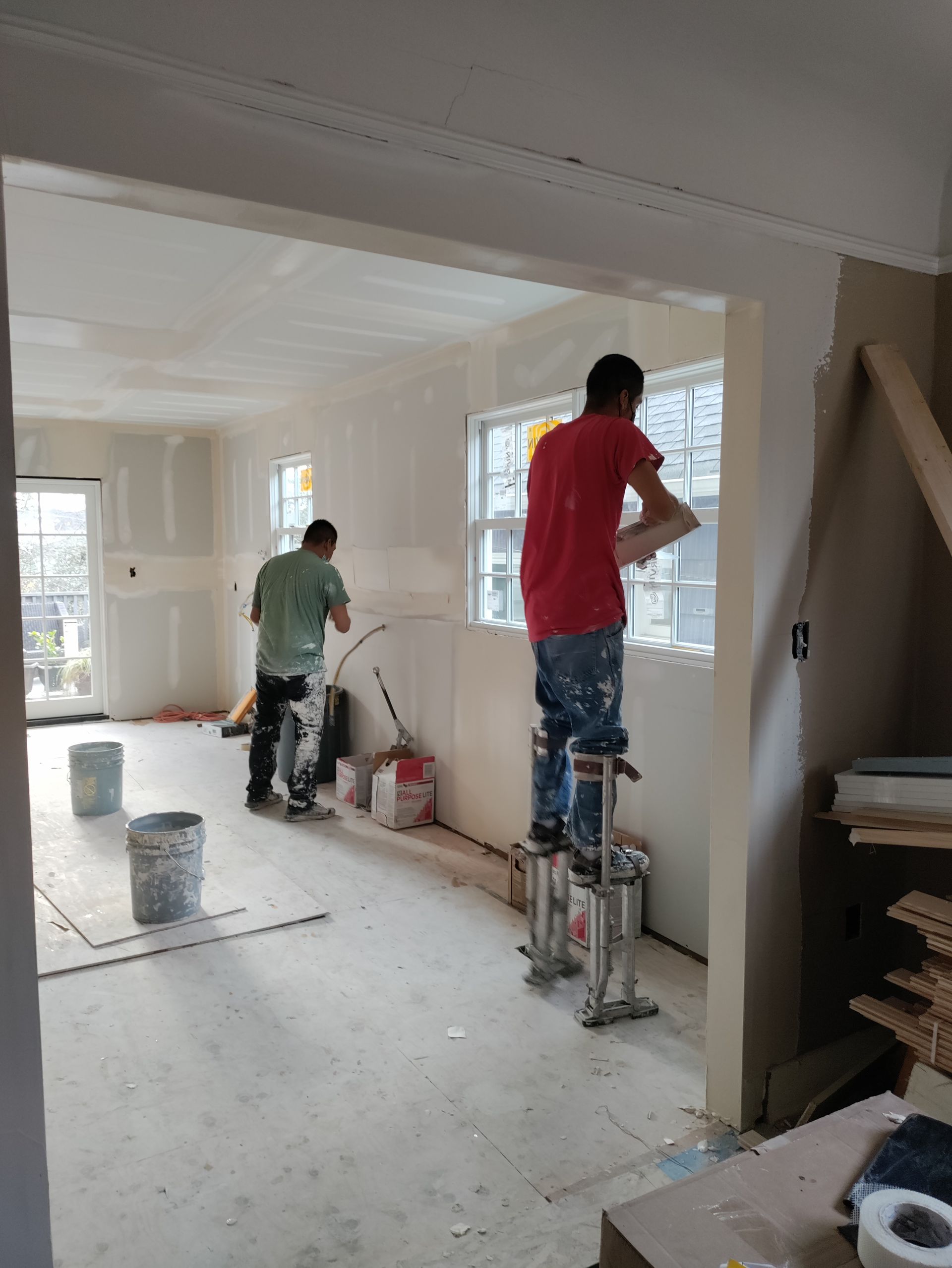 Two workers painting a bright room during renovation, one on a ladder and one near the window.
