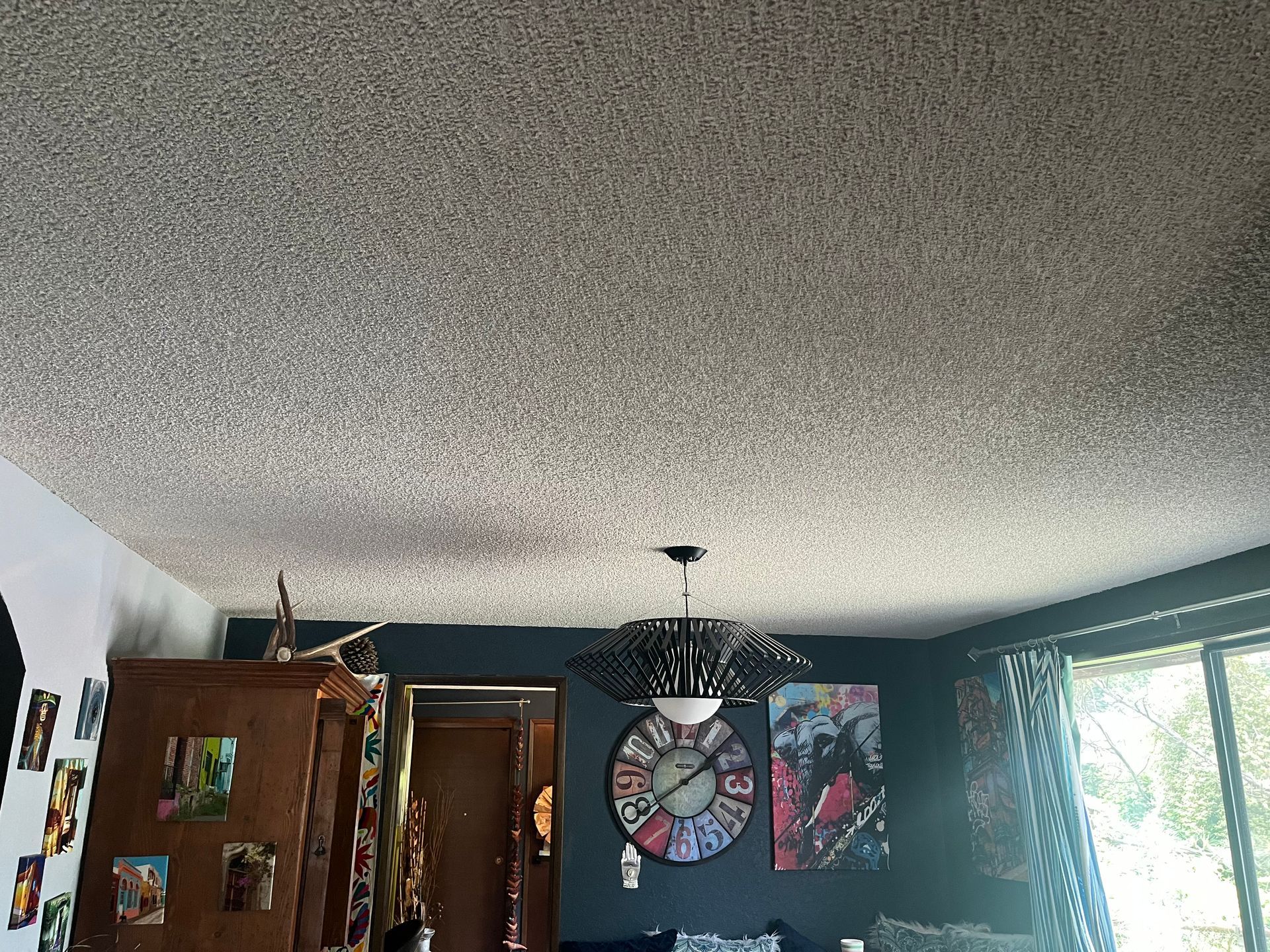 Living room with textured ceiling, wall art, open doorway, and a window letting in bright daylight