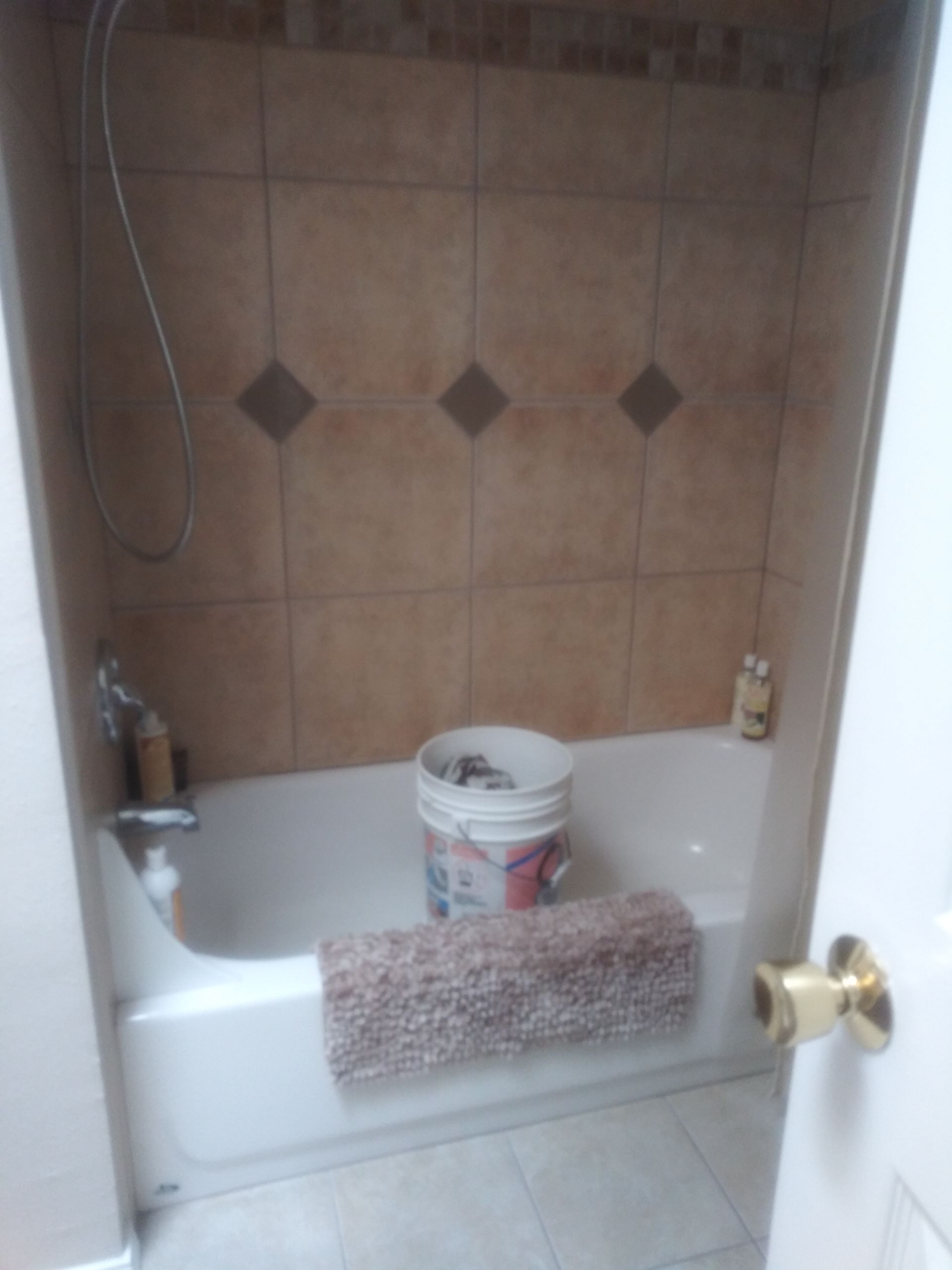 Bathtub in a tiled bathroom with a bucket, towel, and showerhead hanging on the wall.