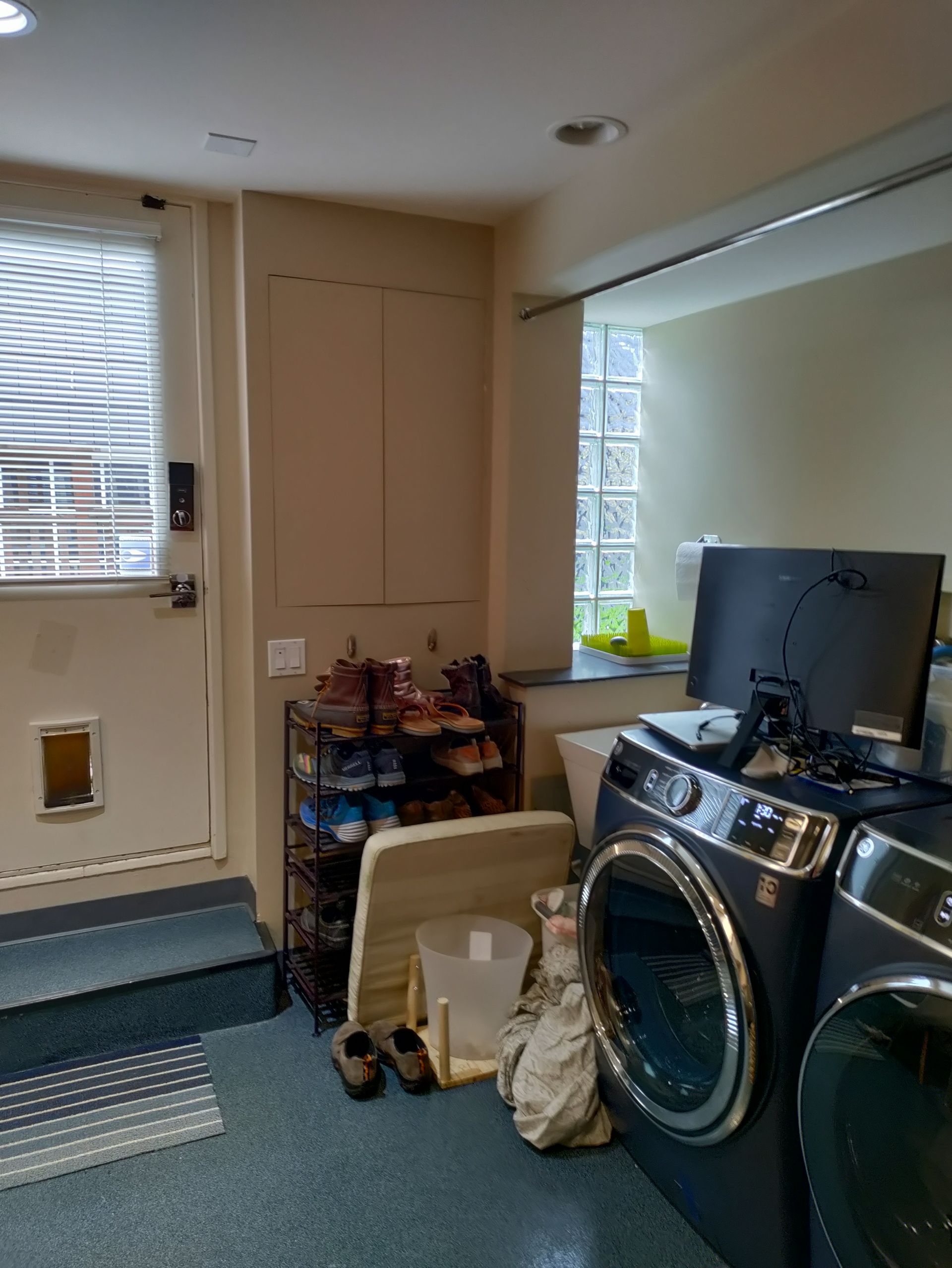 Laundry room with washer, dryer, folded items, and a door with steps and window blinds.