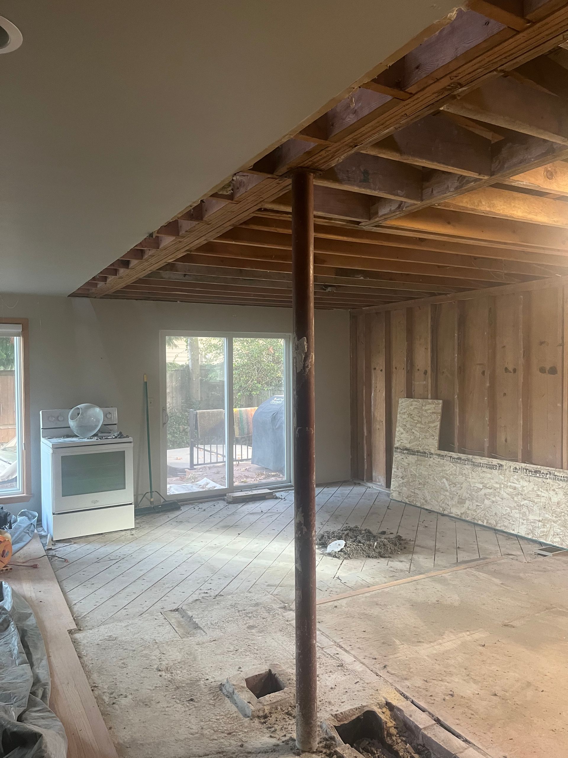 Partially demolished room with exposed beams, debris on floor, and sliding glass doors at the back