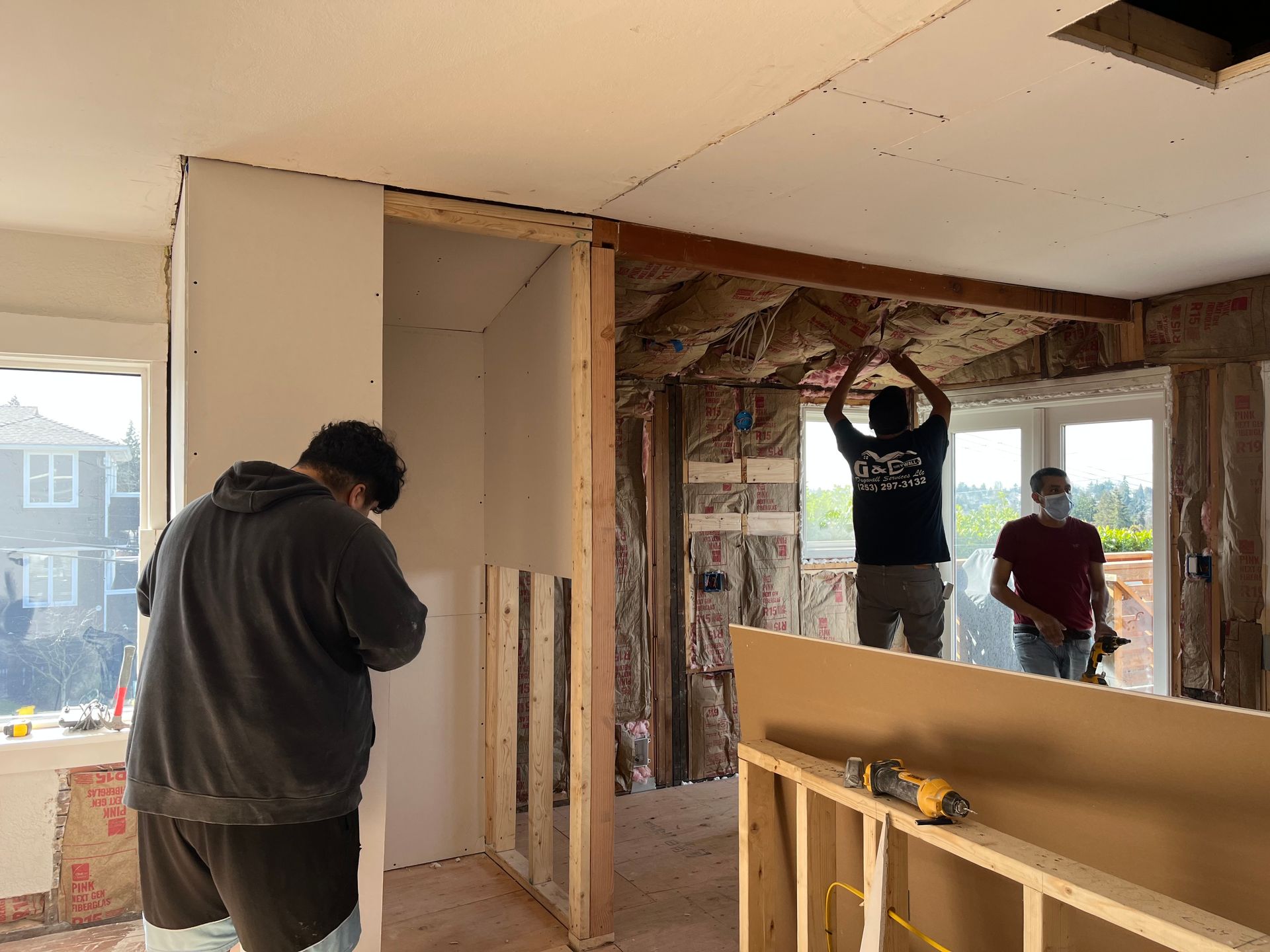 Workers renovating a room, with exposed framing and a person installing overhead supports.