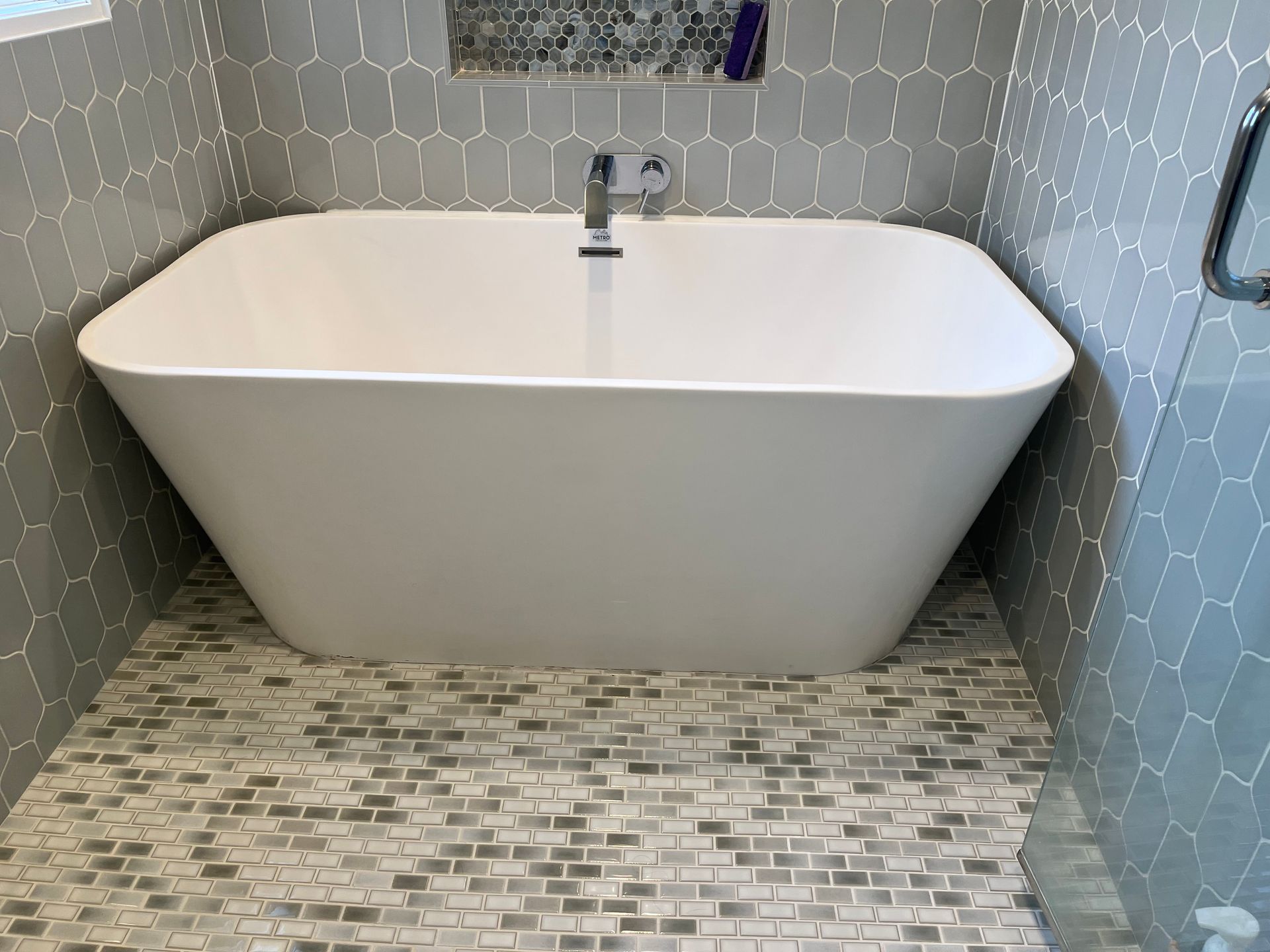 Modern white bathtub in a tiled bathroom with gray patterned walls and floor.