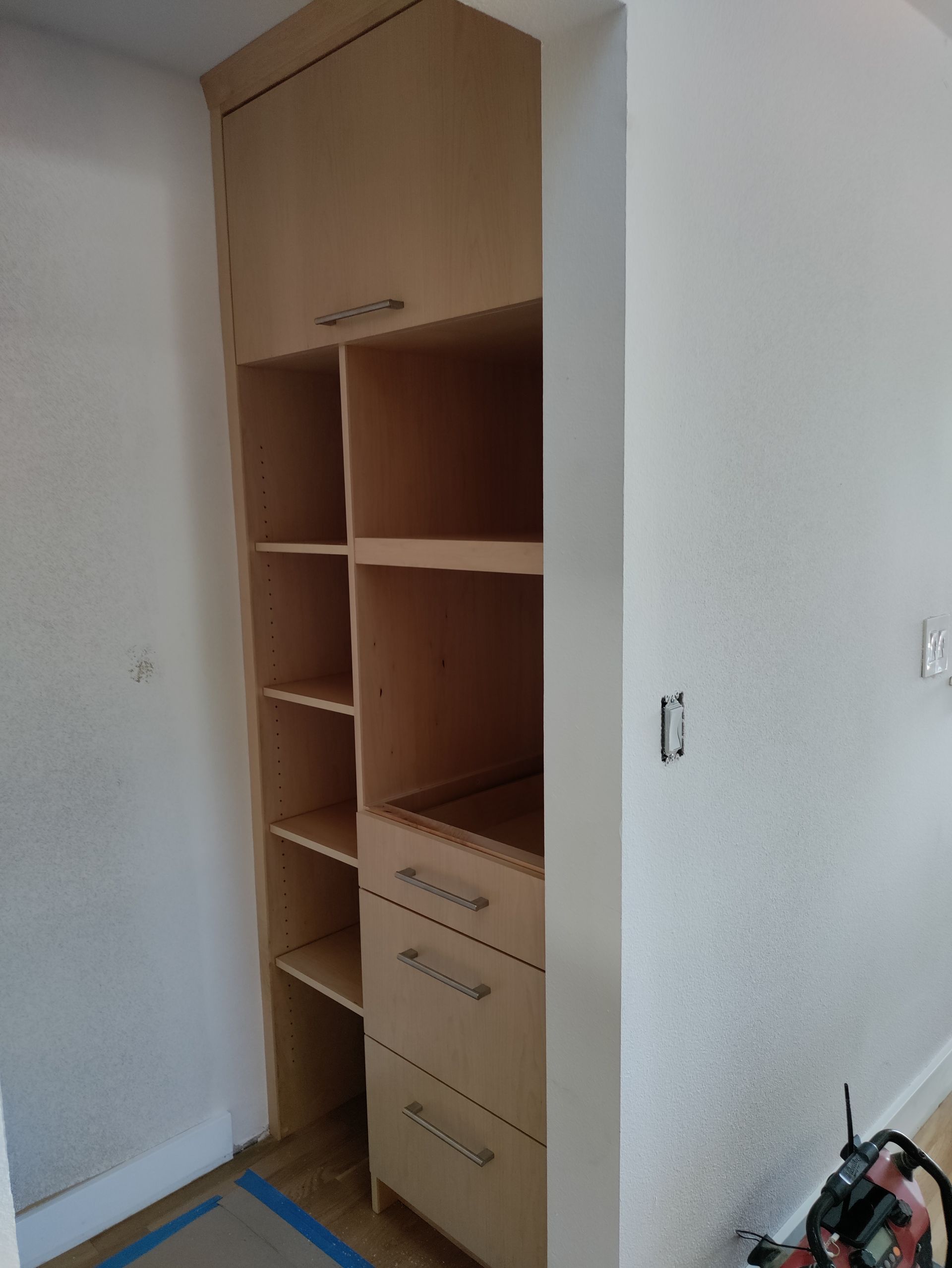 Built-in wooden wardrobe in a small white room, with open shelves and drawers under construction.