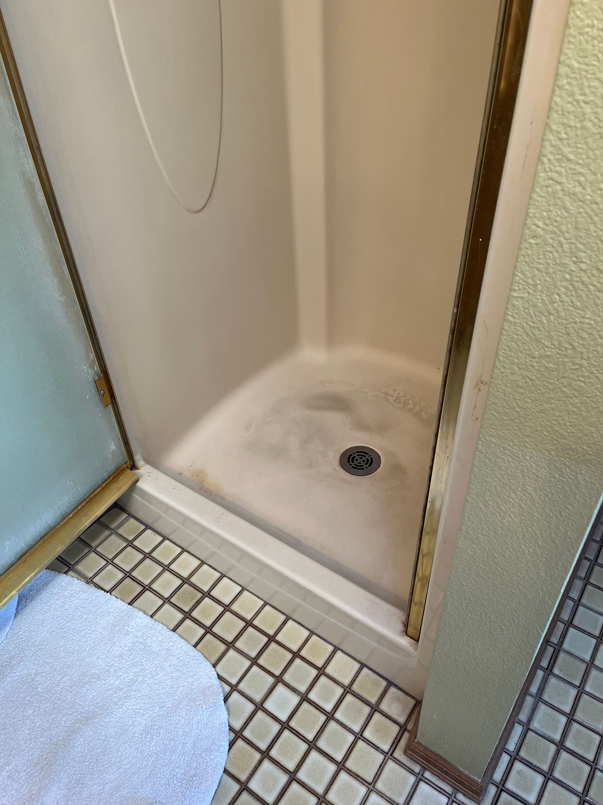 Small tiled shower stall with a drain, viewed from a bathroom doorway.