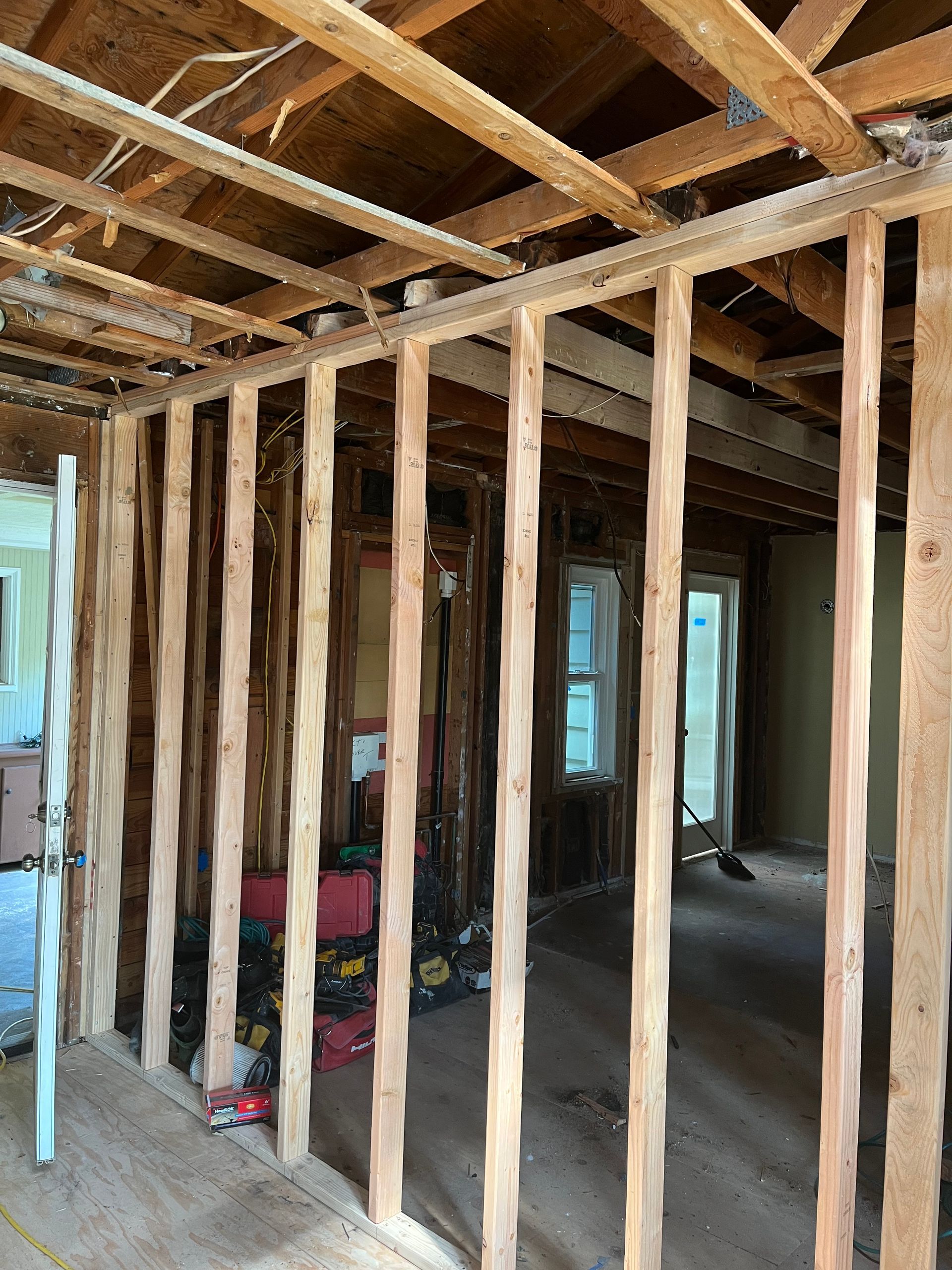 Unfinished room framing with exposed wooden studs and ceiling joists, windows visible in the background.