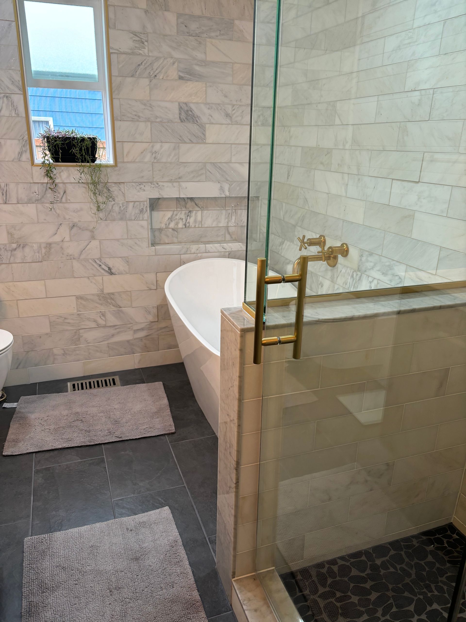 Modern bathroom with a freestanding tub, glass shower partition, and gray rugs on tiled floor