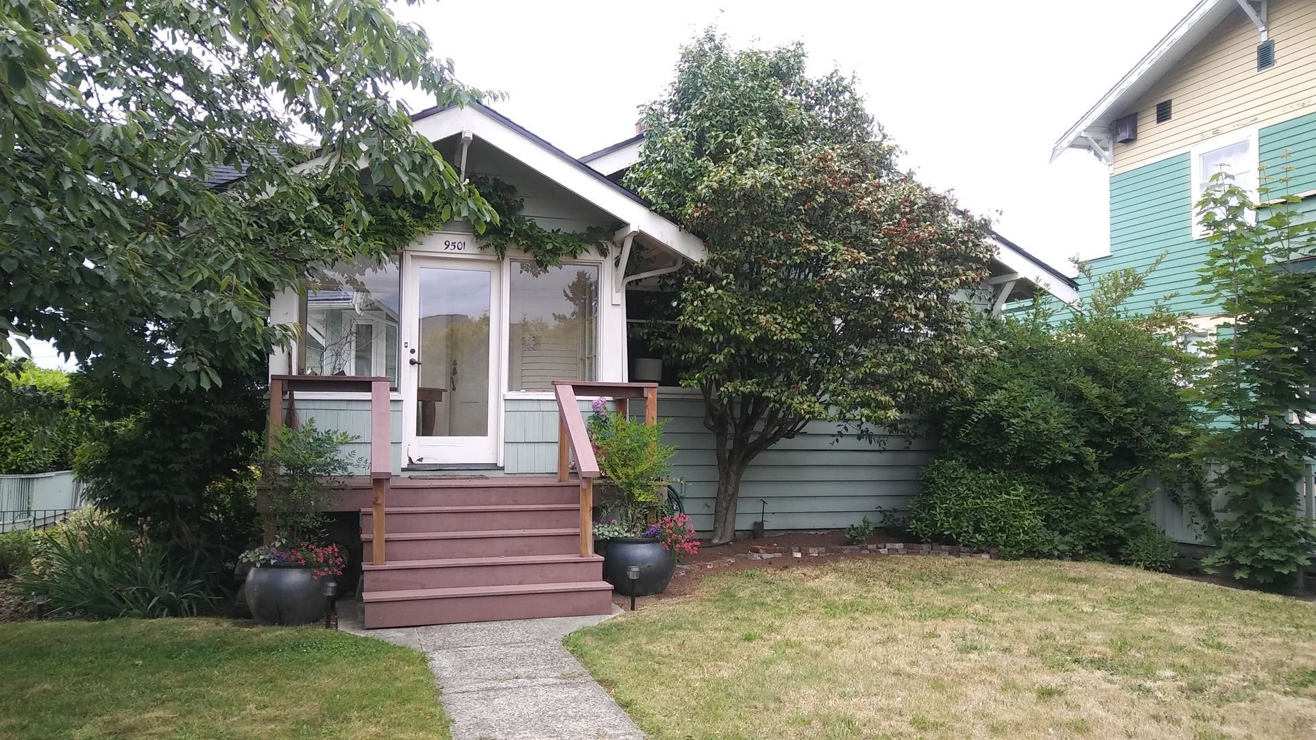 Small front porch with steps, white trim, garden plants, and a gravel path leading through a lawn.