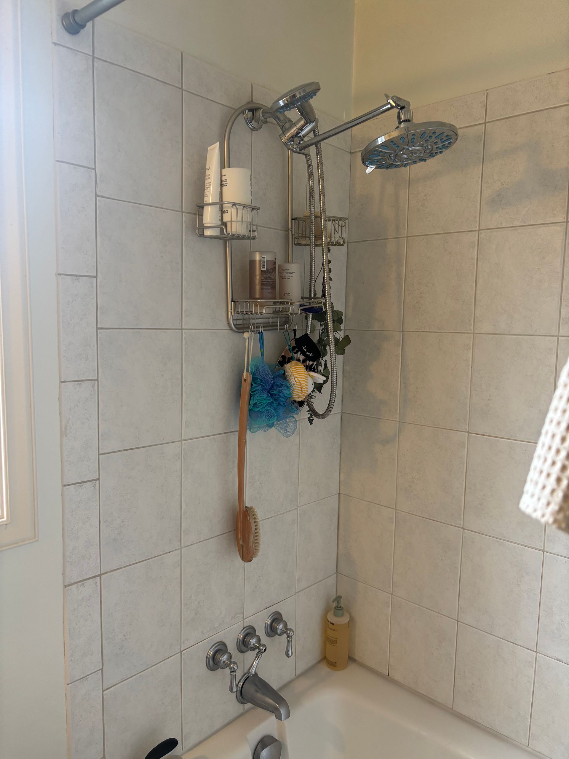 Shower corner with chrome showerhead, tiled walls, and hanging bath items