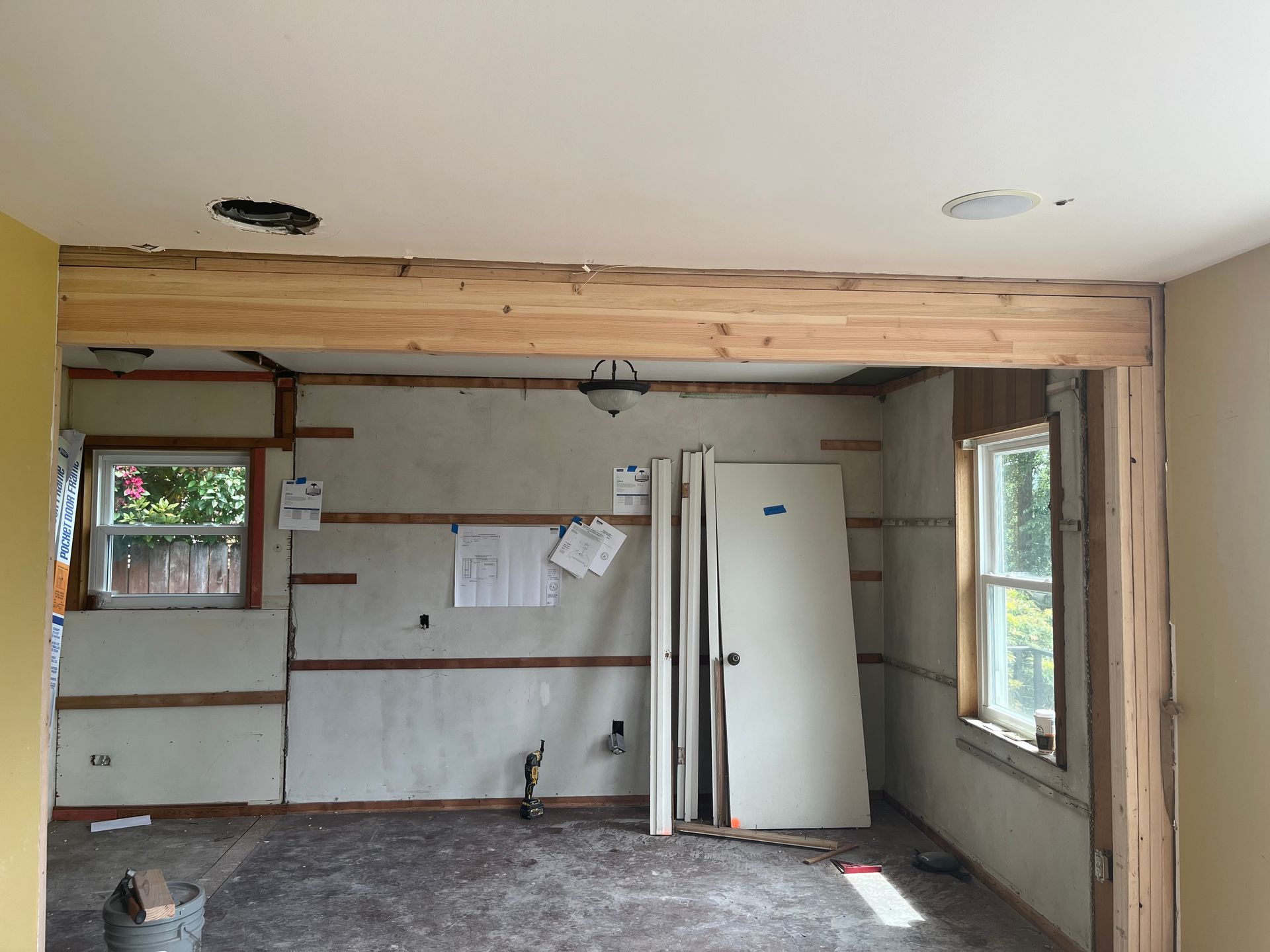 Partially renovated kitchen with exposed wood beam, white fridge, and windows on the right