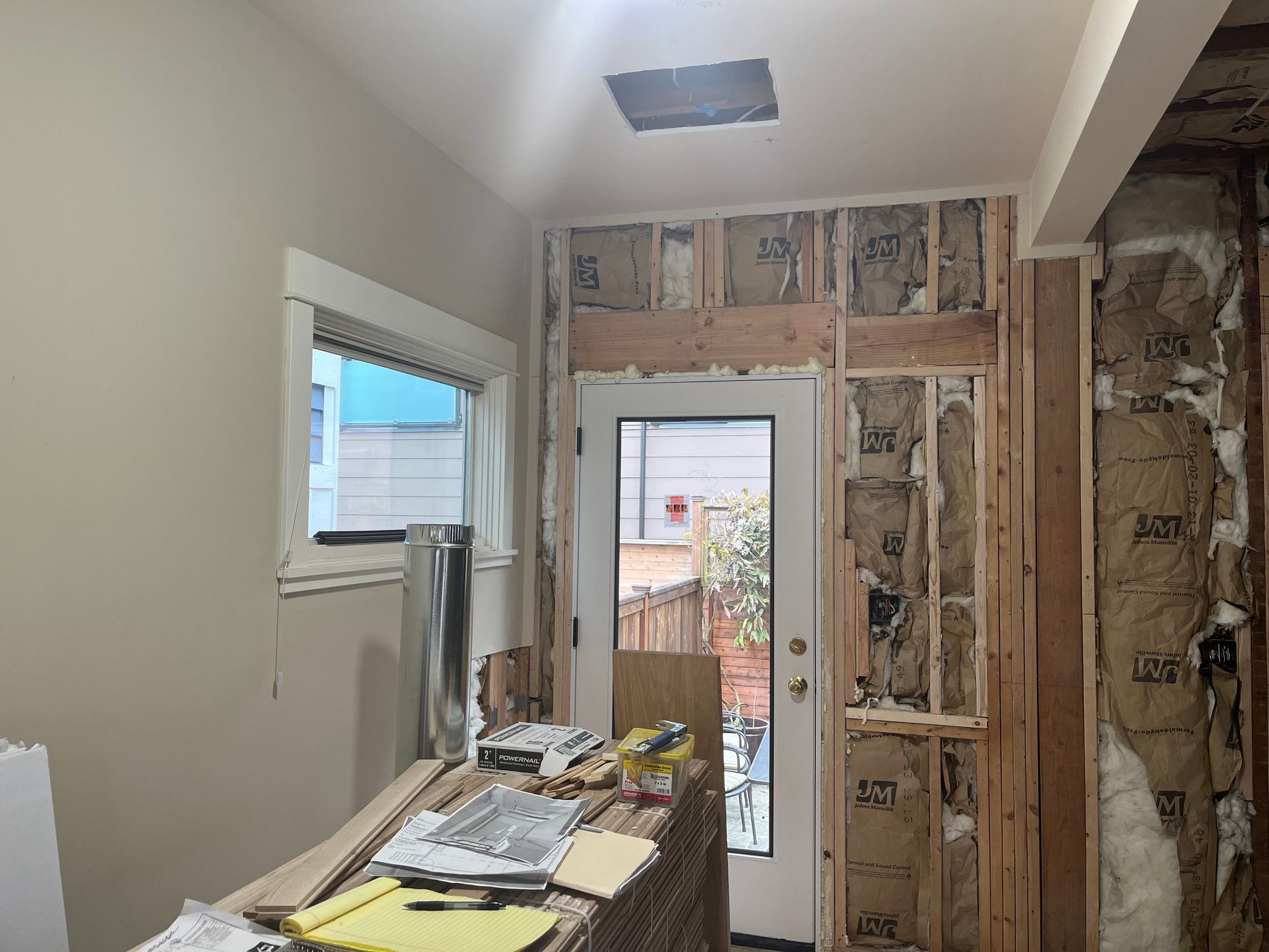 Renovated hallway with exposed walls, a door to outside, and construction materials on a worktable.