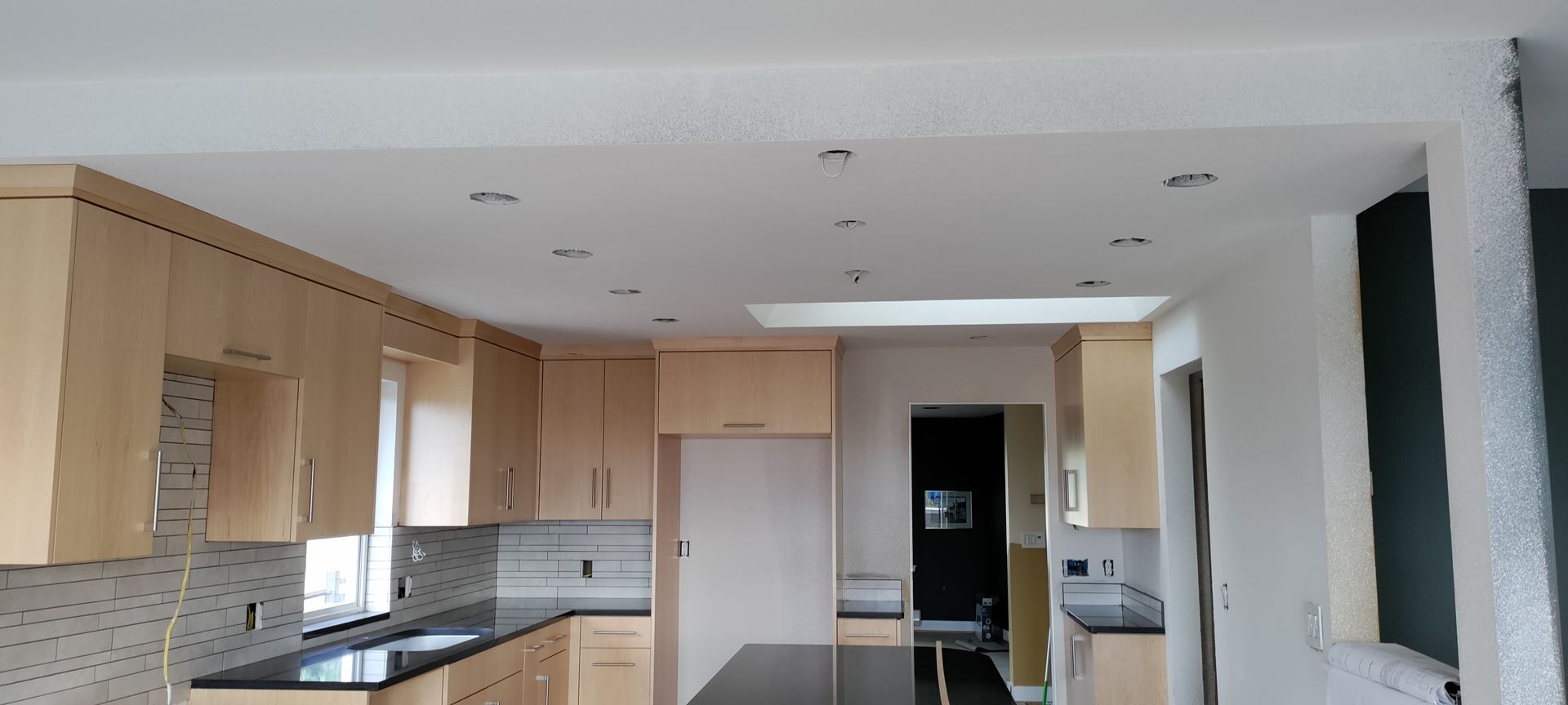 Modern kitchen with light wood cabinets, black countertops, and a white ceiling in a bright room