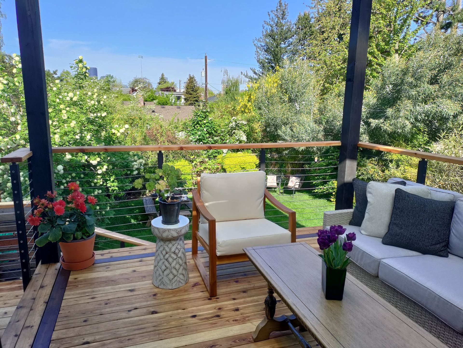 Sunny garden deck with cushioned chairs, potted flowers, and a view of lush greenery