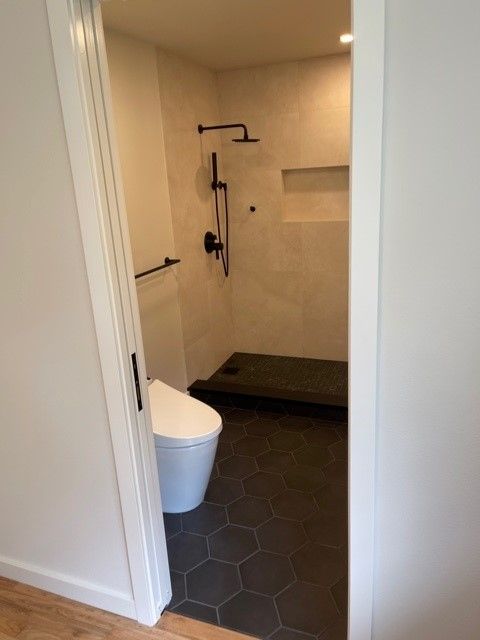 Modern bathroom with white walls, black hex tile floor, and a walk-in shower with dark fixtures.