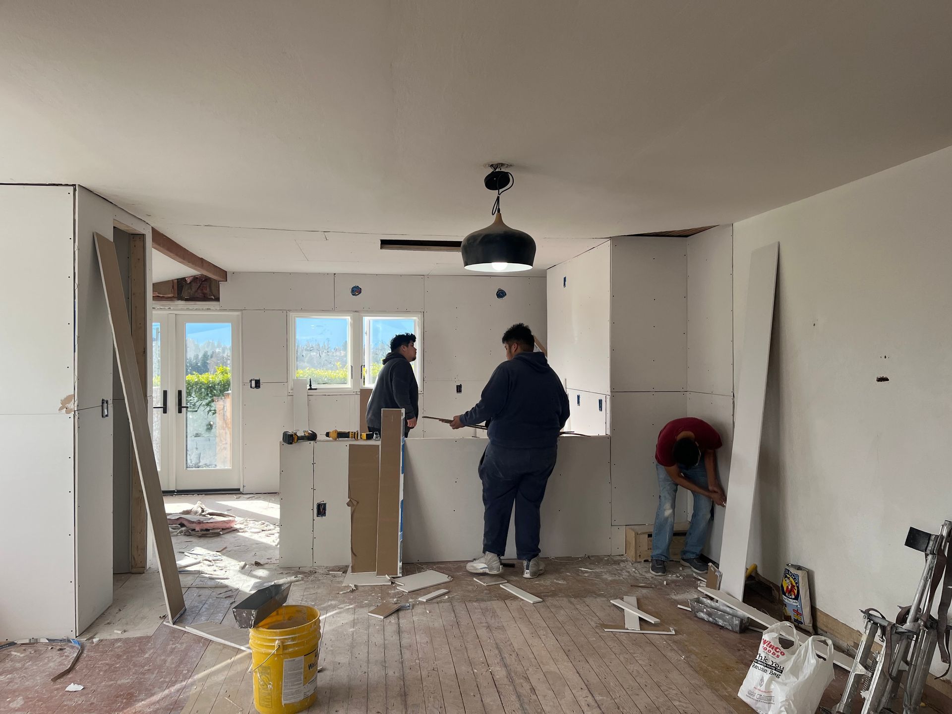 People working in a partially renovated kitchen with exposed walls and debris on the floor.