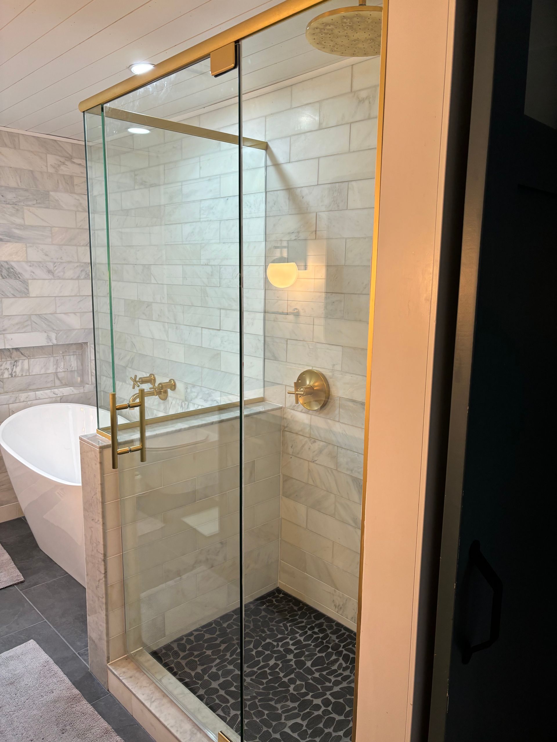 Glass-enclosed shower with gold fixtures beside a freestanding tub in a tiled bathroom