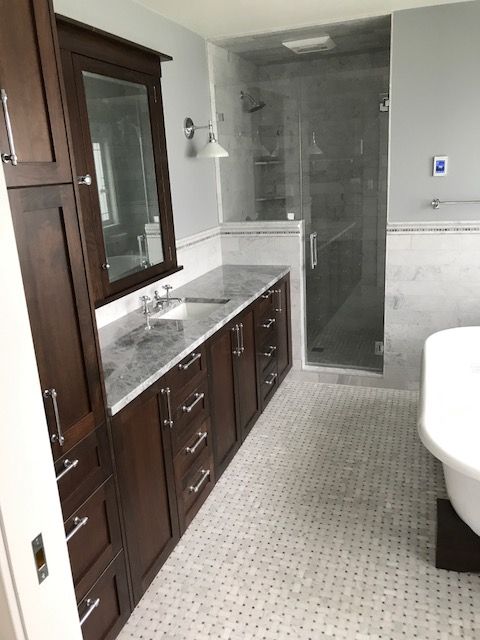 Modern bathroom with dark wood vanity, white sink, gray tiled shower, and mosaic floor