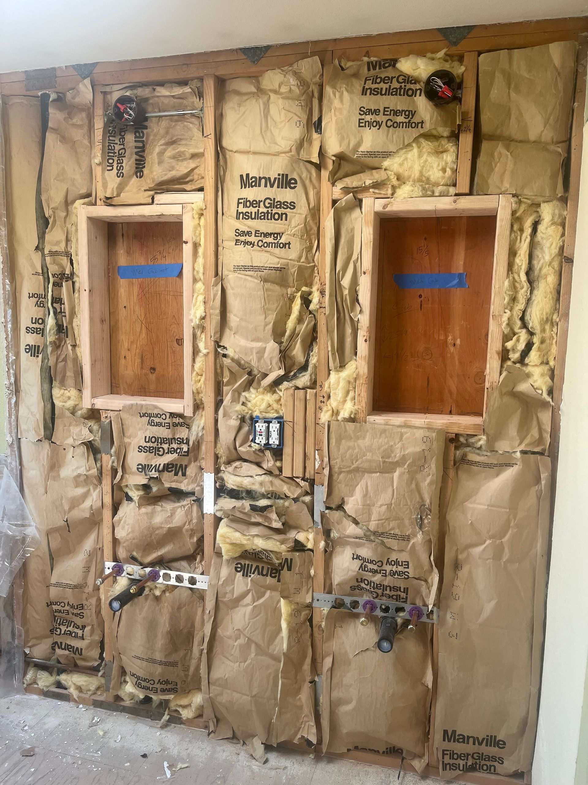Insulated wall with two framed window openings, exposed studs, and handwritten notes on kraft paper barriers
