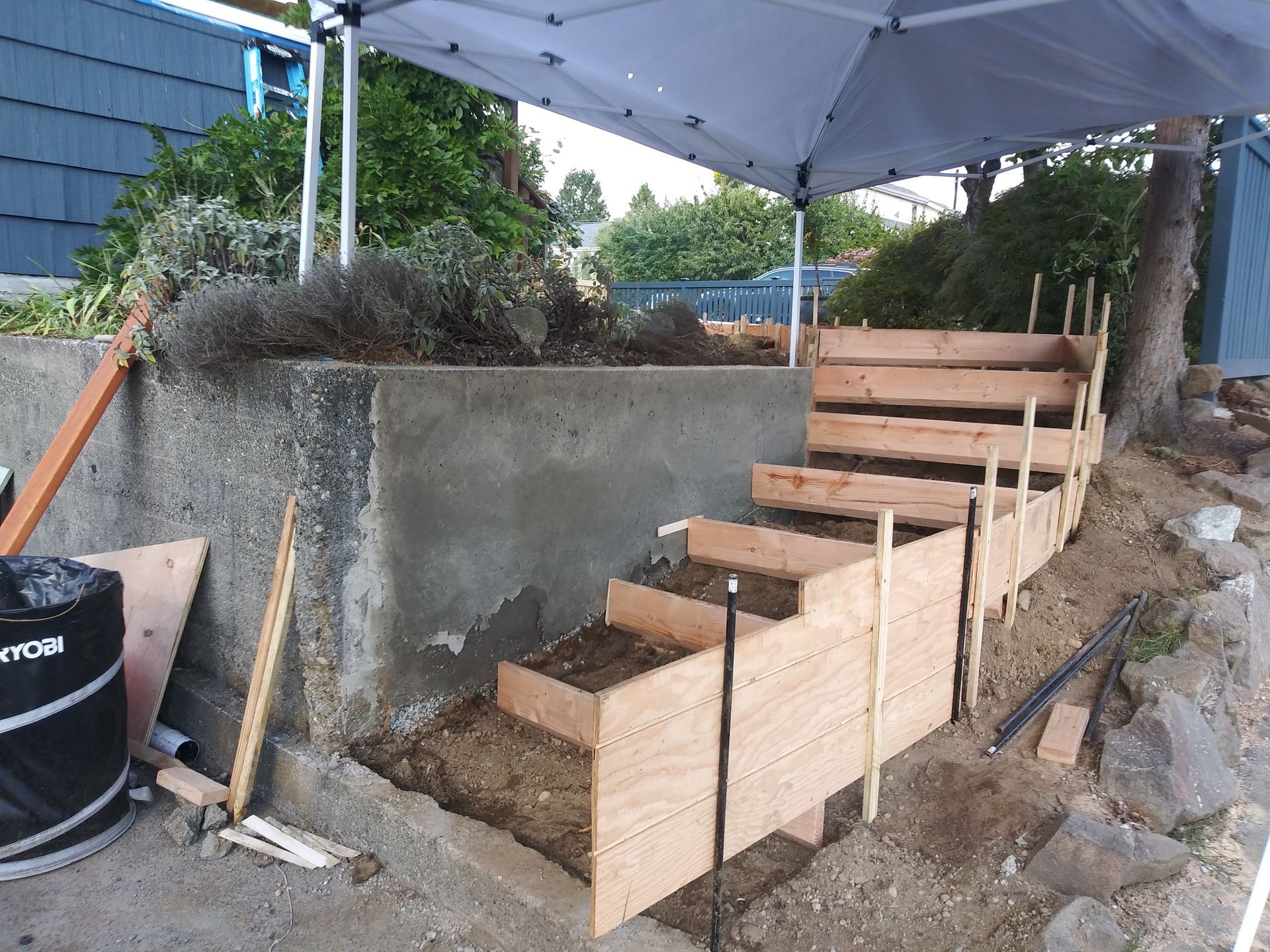 Wooden steps built into a dirt slope beside a concrete wall under a canopy.