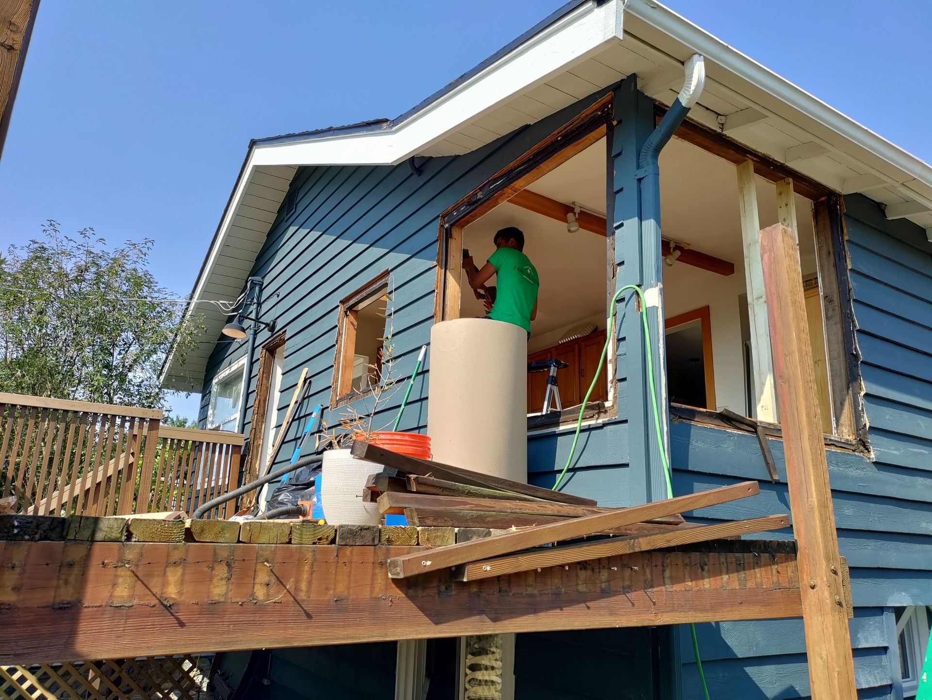 Worker painting a blue house exterior on a wooden deck during renovation