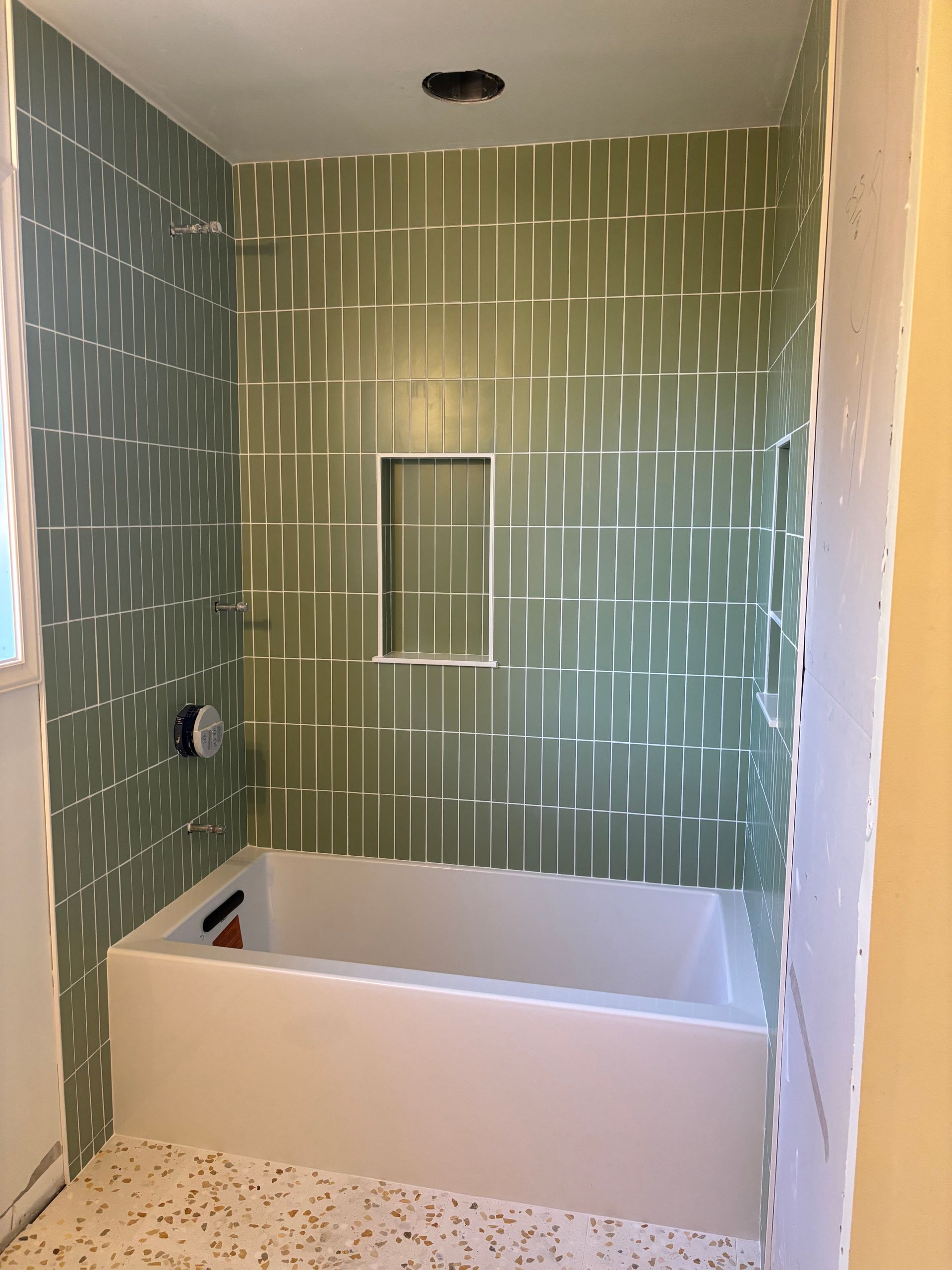 Bathroom tub alcove with green tile walls and unfinished white tub surround
