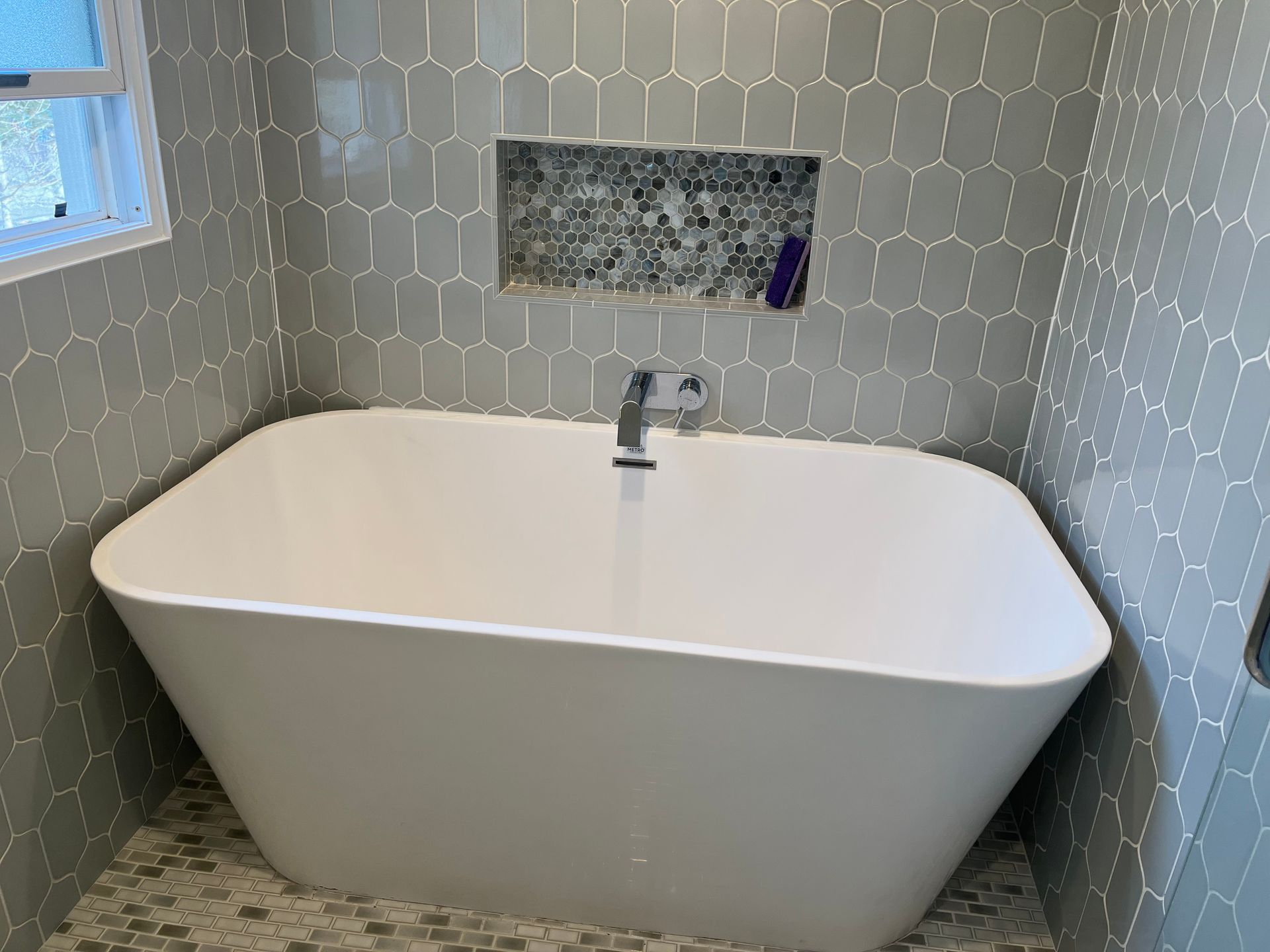 Modern white bathtub with chrome faucet in a tiled bathroom