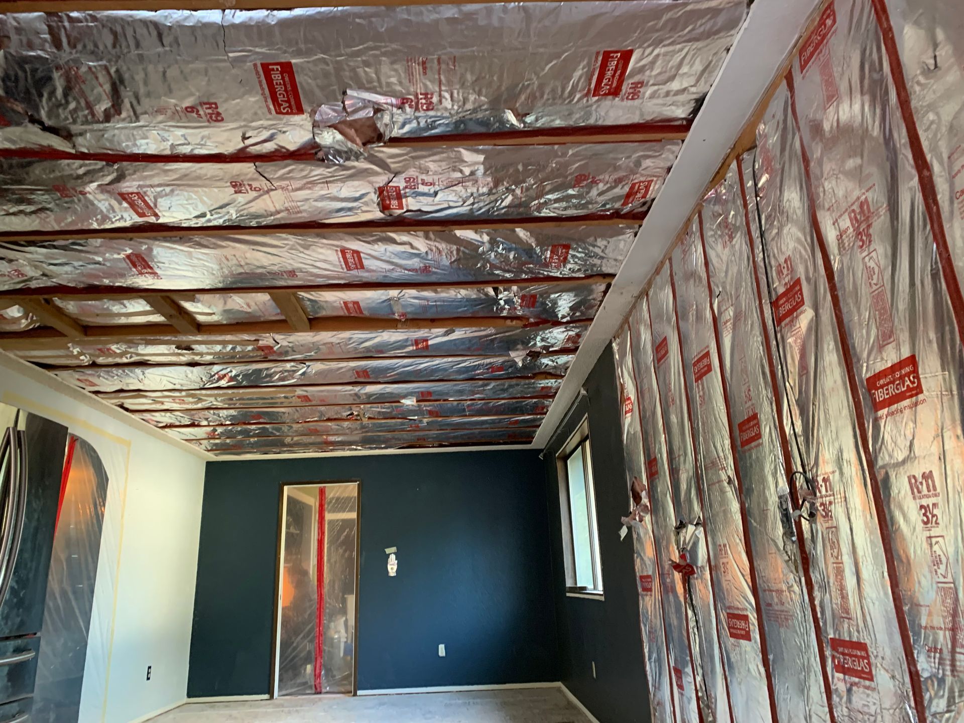Renovated room with reflective ceiling insulation, dark accent wall, and exposed window openings.