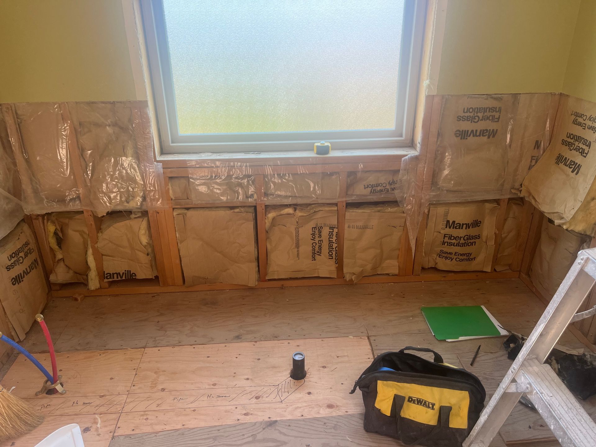 Partially insulated room with a frosted window, exposed wall framing, and a tool bag on the floor