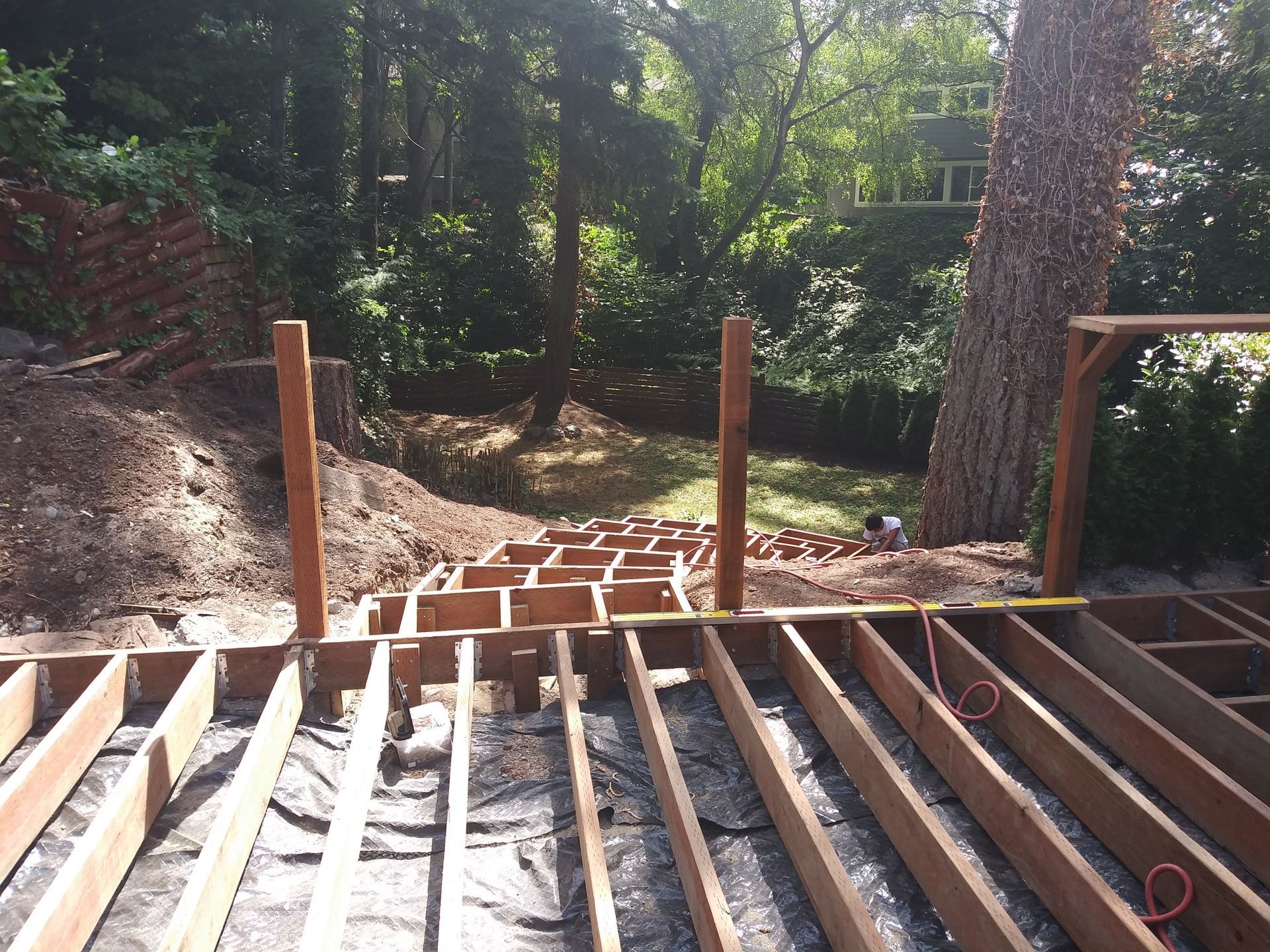 Partially built wooden deck overlooking a wooded backyard, with exposed joists and posts