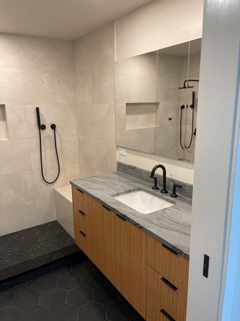 Modern bathroom with gray tile, wood vanity, black fixtures, mirror, and accessible shower bench