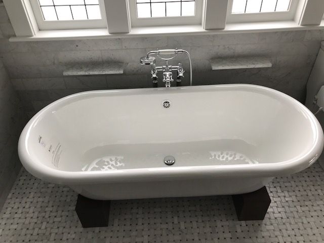 Modern white freestanding bathtub beneath a chrome faucet in a tiled bathroom