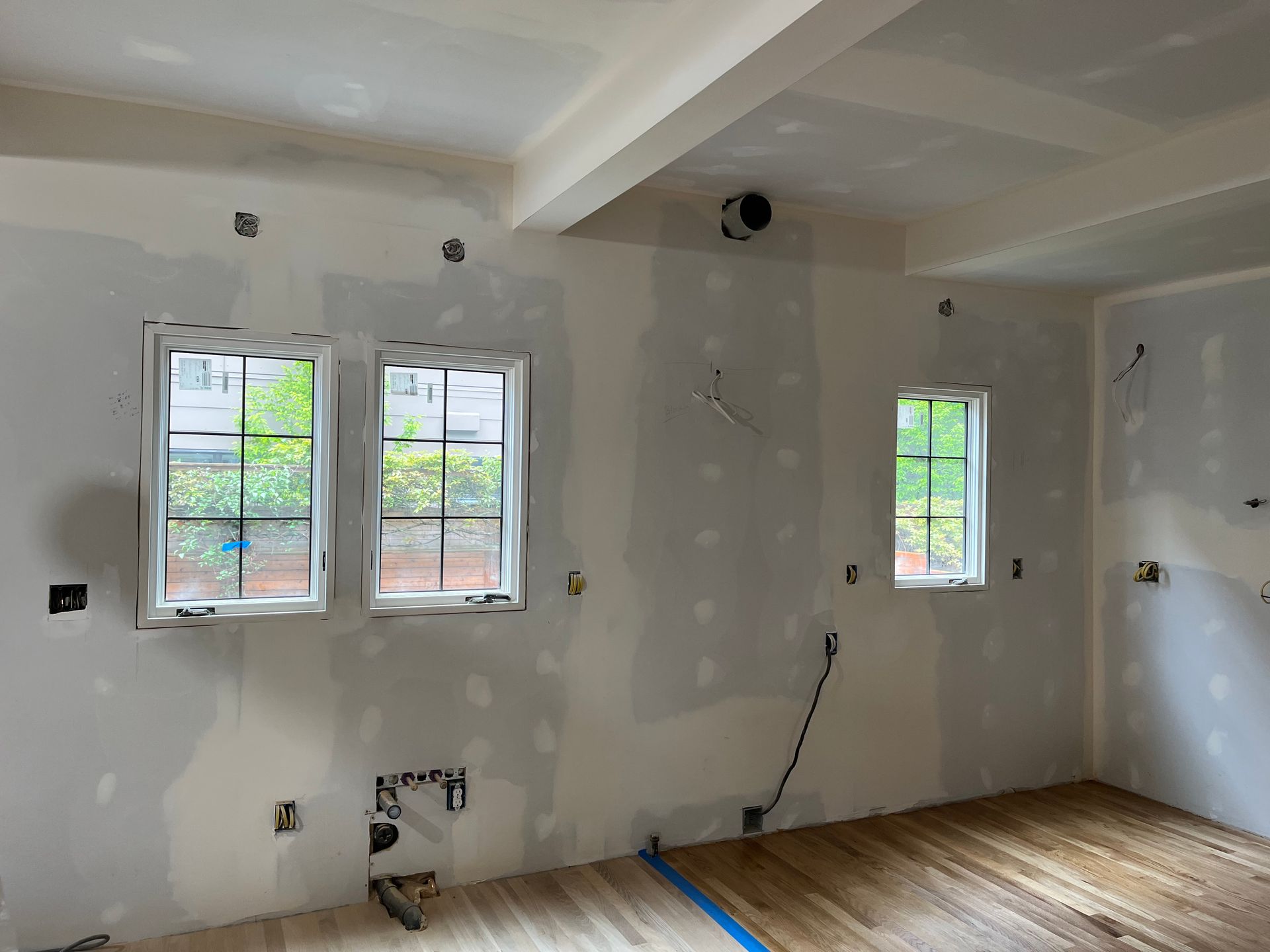 Renovated room with white walls, exposed outlets, three windows, and hardwood floor under construction