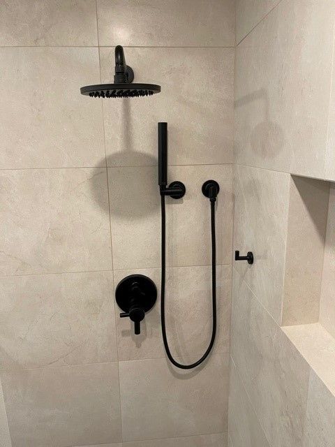Modern beige-tiled shower with black rainfall head, handheld wand, and control fixtures
