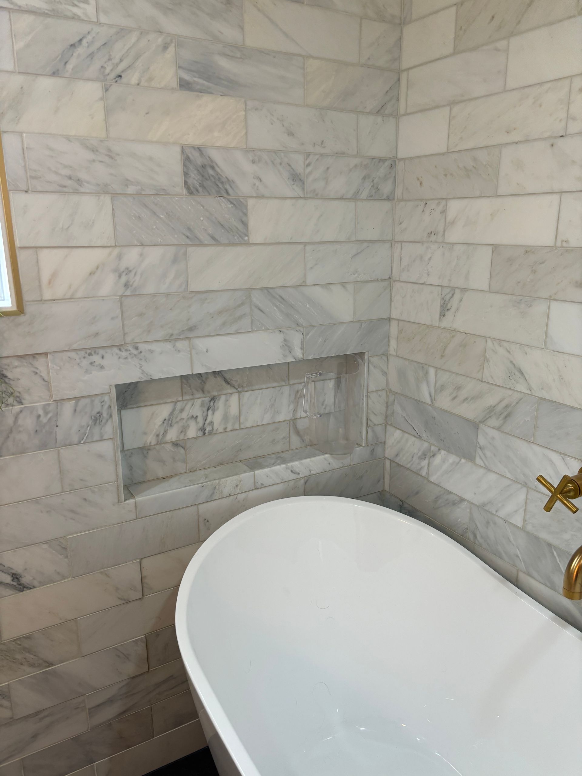 Marble-tiled bathroom with a built-in wall niche and a white bathtub under a window