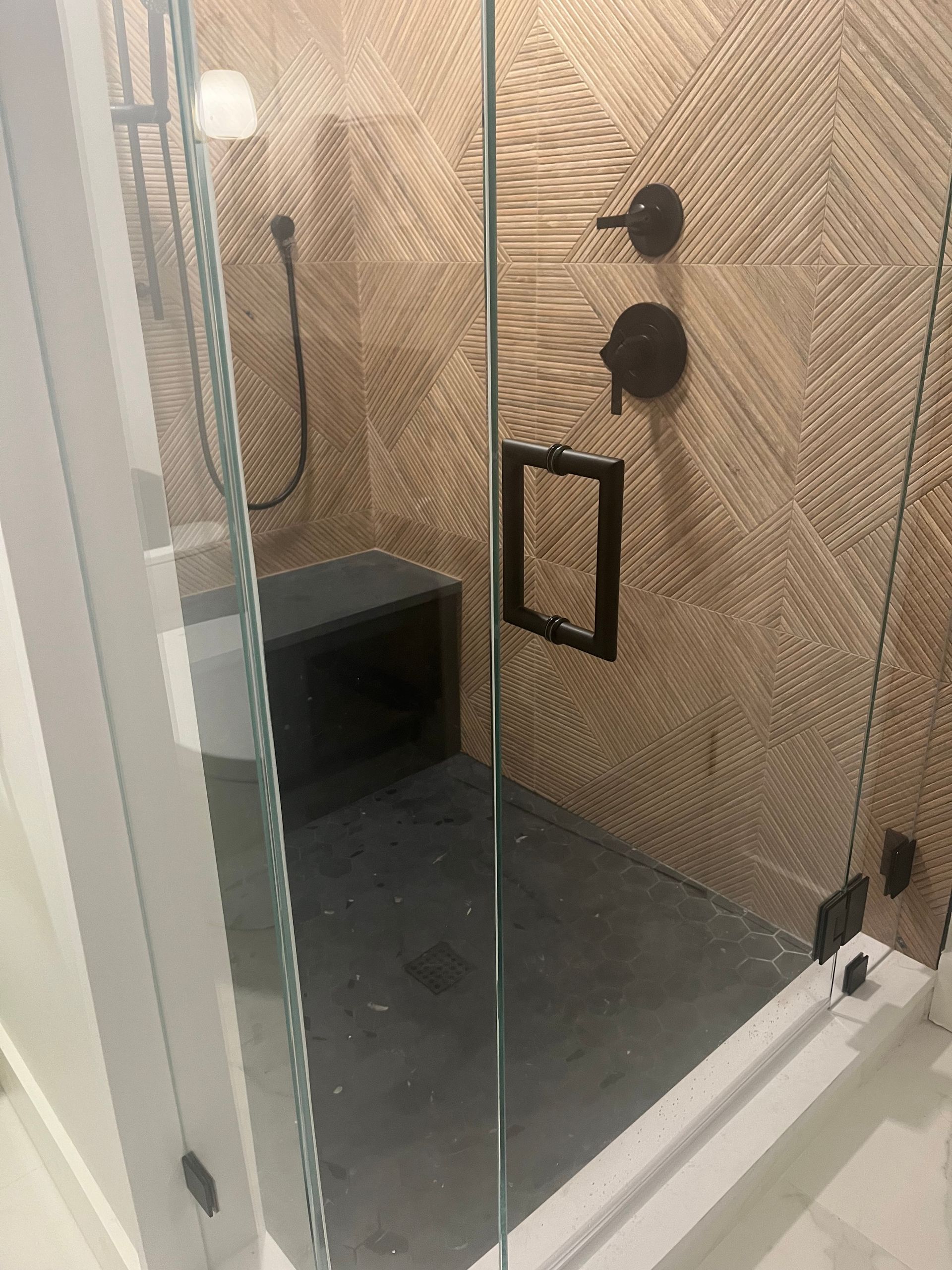 Glass shower enclosure with black fixtures and beige patterned tile walls