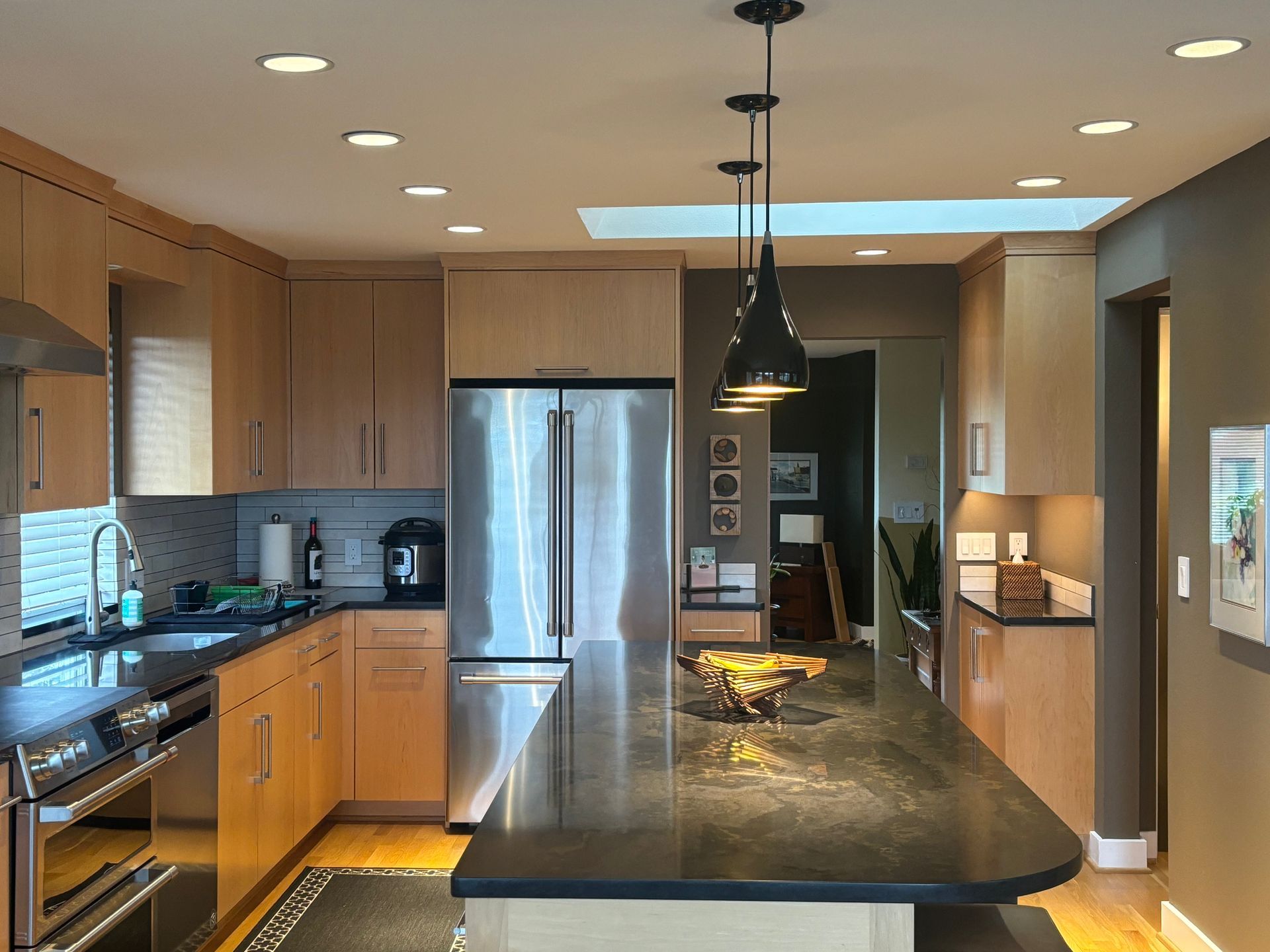 Modern kitchen with wood cabinets, stainless steel fridge, and a large island under pendant lights.