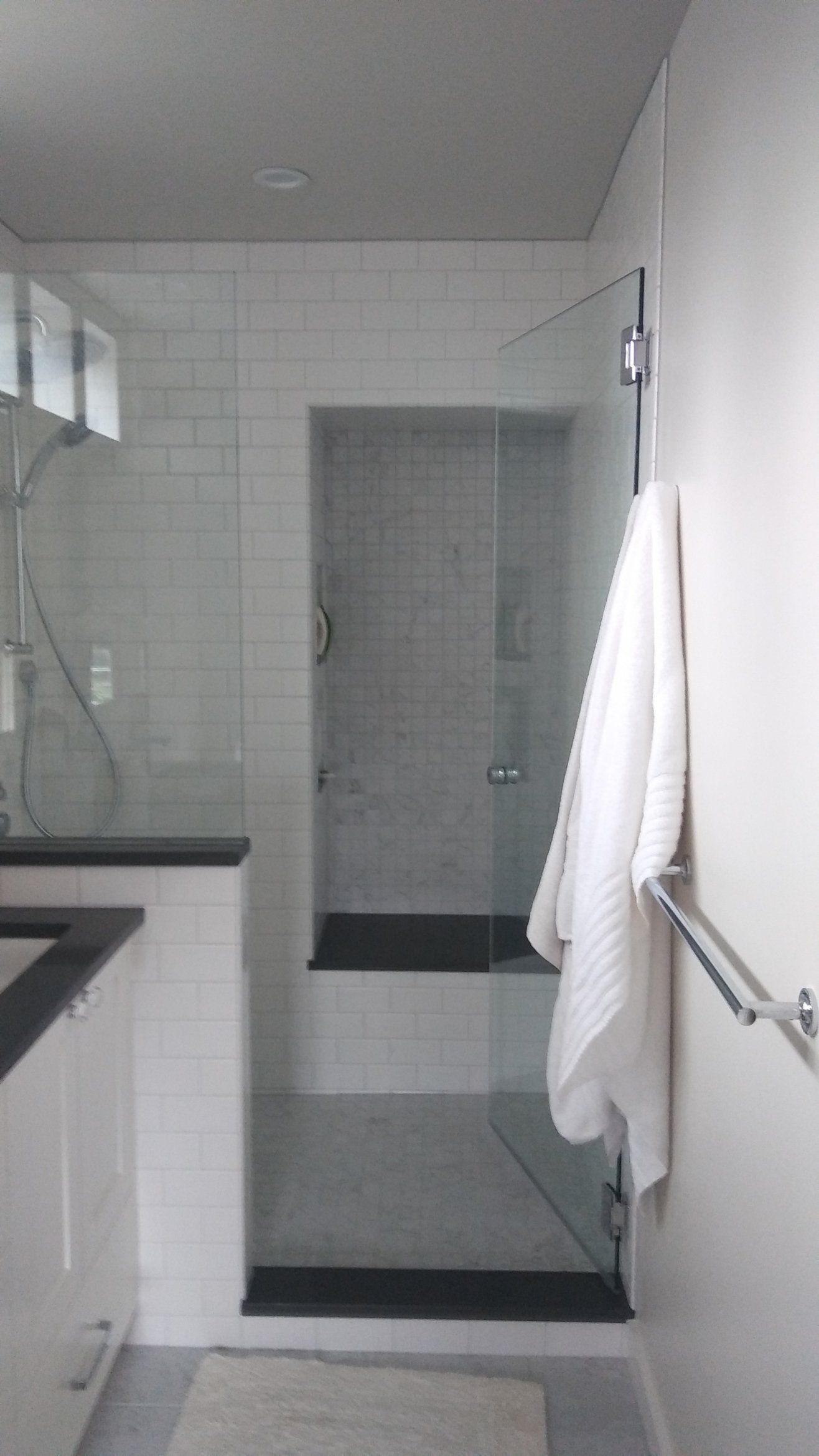 Small tiled bathroom with a glass shower door, white towel, and countertop sink on the left.