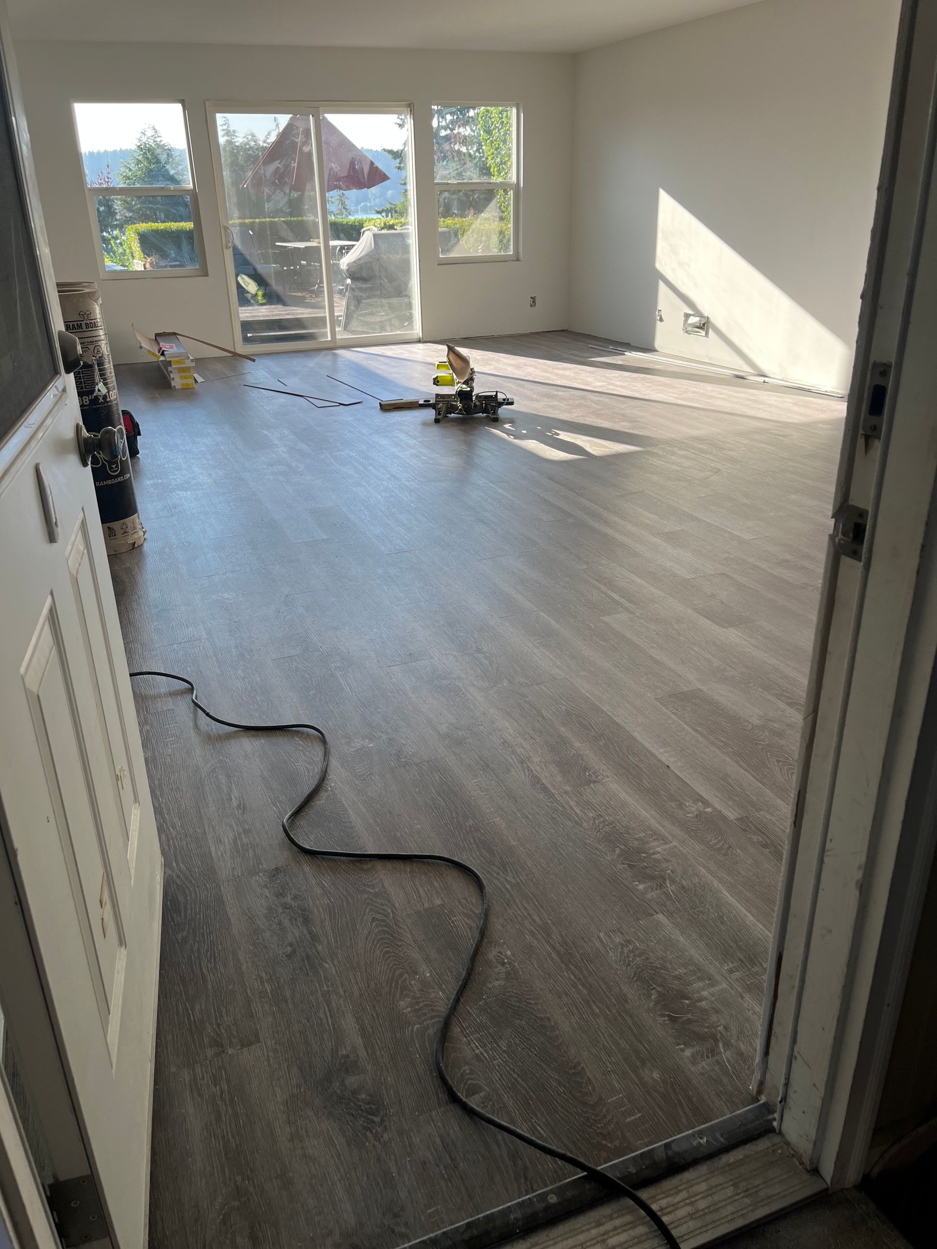 Empty bright room with new flooring, sunlight from windows, and a power cord across the floor.