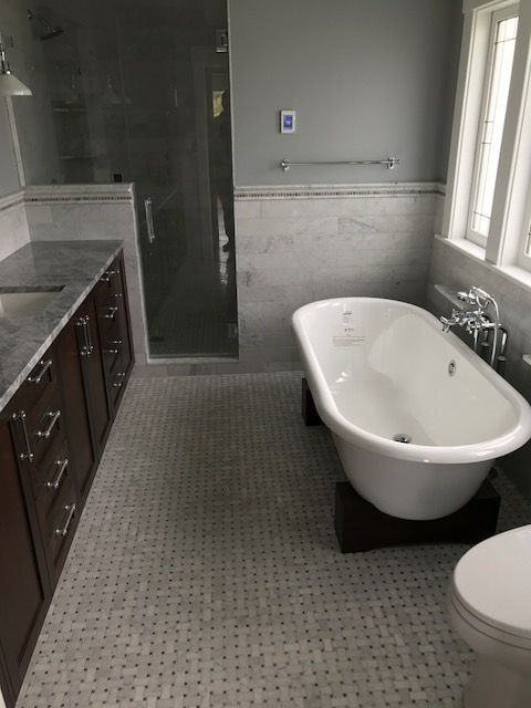 Bathroom with freestanding white bathtub, glass shower, dark vanity, and gray tile floor.