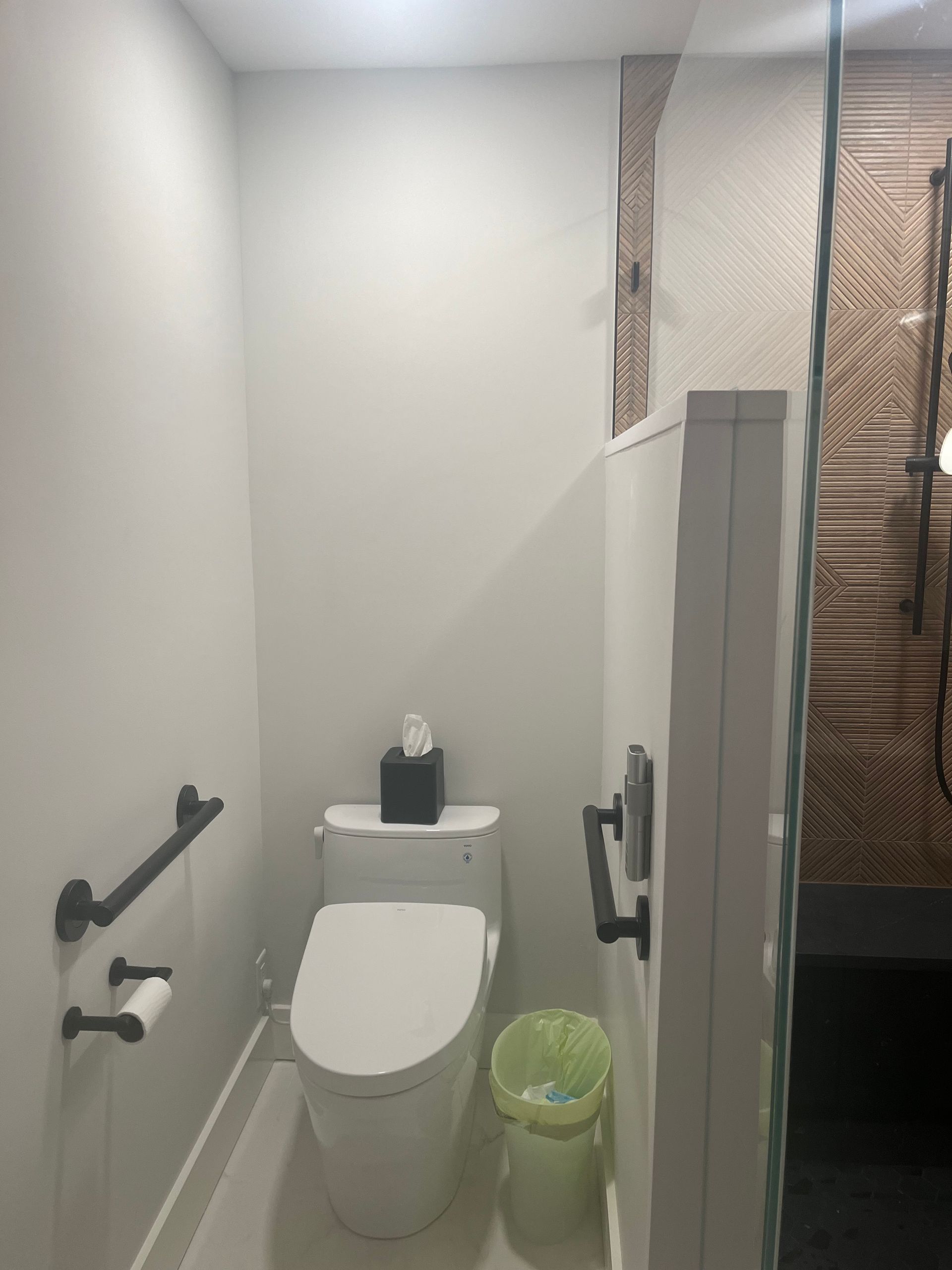Small restroom with a toilet, grab bars, trash bin, and partially open shower curtain.